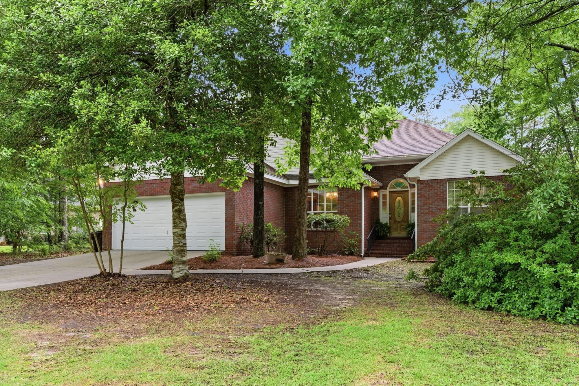 Red-brick house with a white garage, framed by mature trees and greenery.