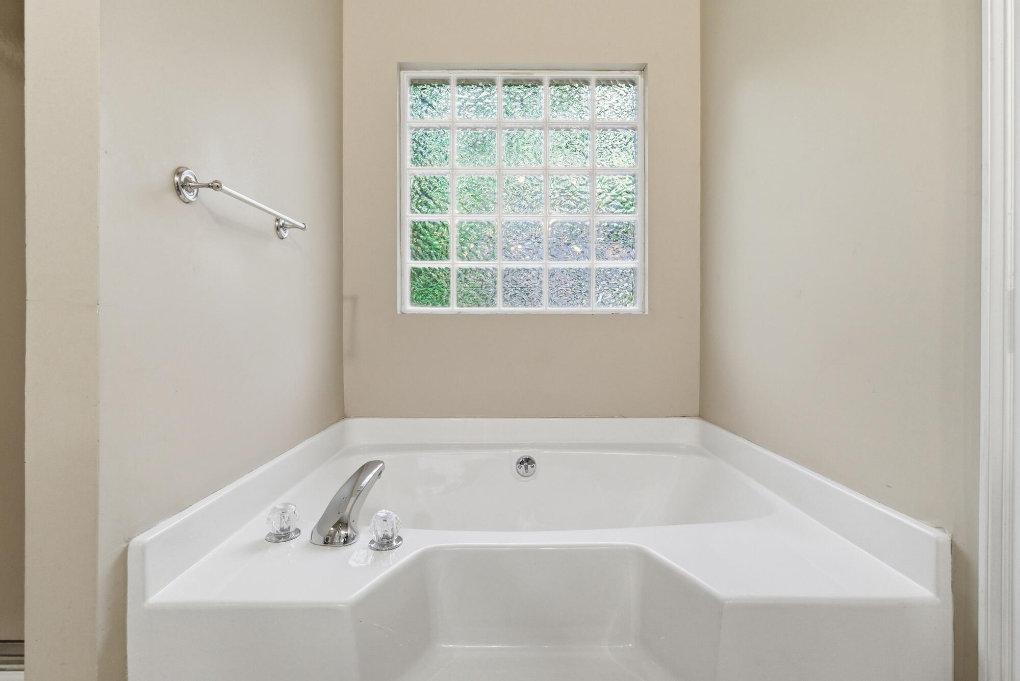 Corner bathtub beneath a glass-block window, with chrome fixtures and a wall-mounted grab bar.