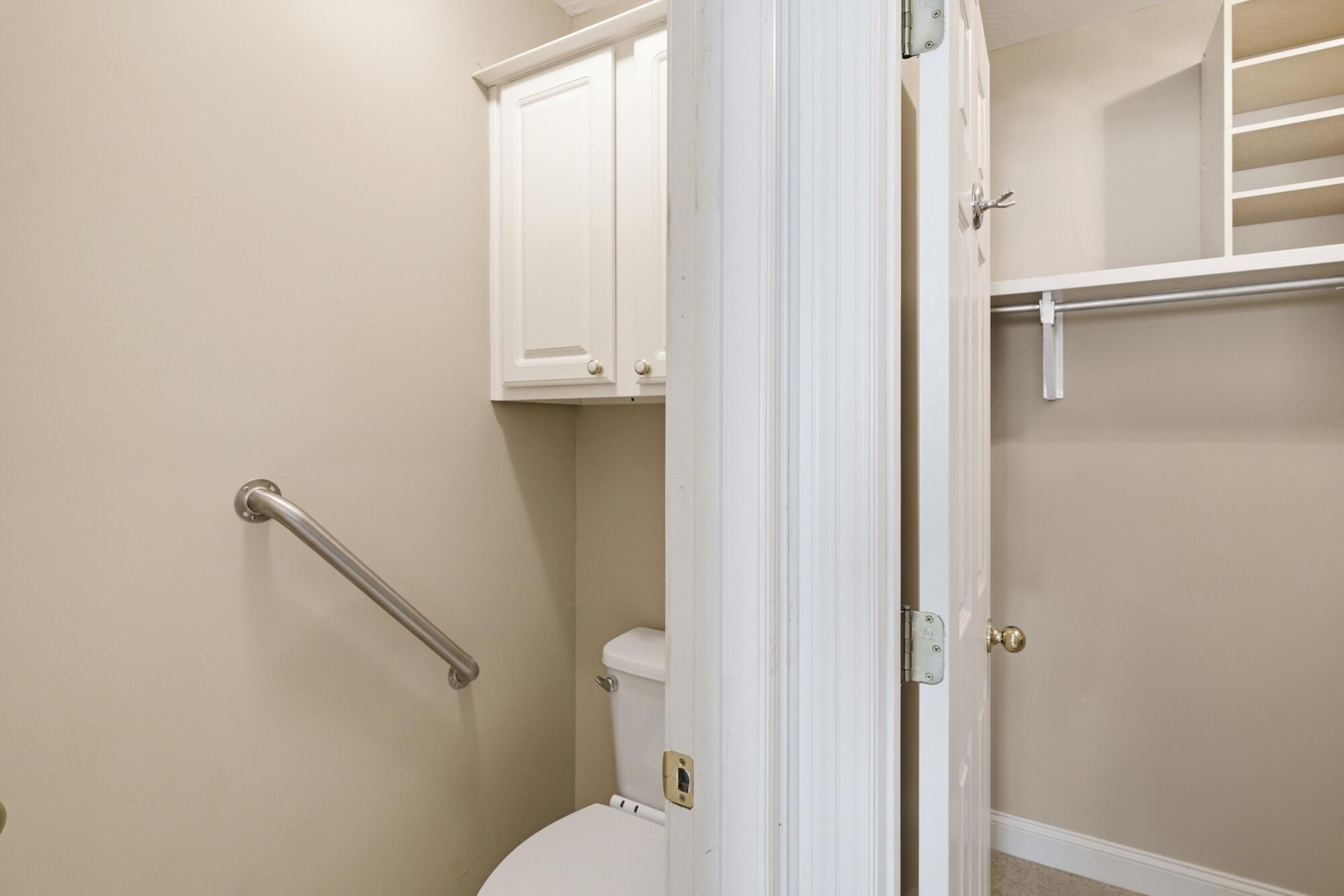Bathroom with a stainless grab bar, partially screened toilet, and adjacent open closet.
