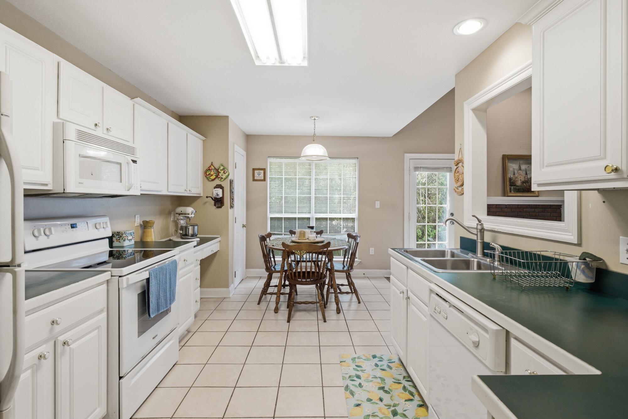 Kitchen with white cabinets, dark green countertops, a double sink, and a dining table by large windows.