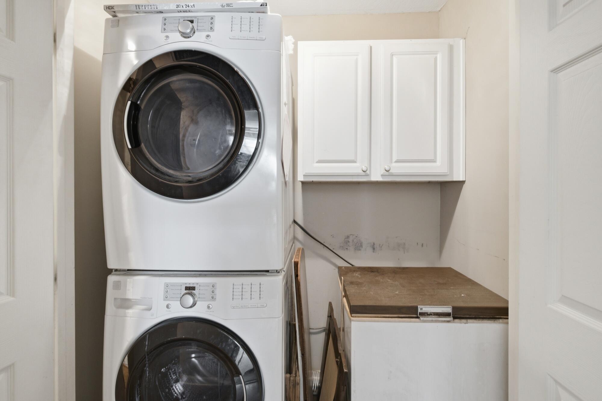 Stacked white front-loading washer and dryer beside a wall cabinet and wooden countertop.
