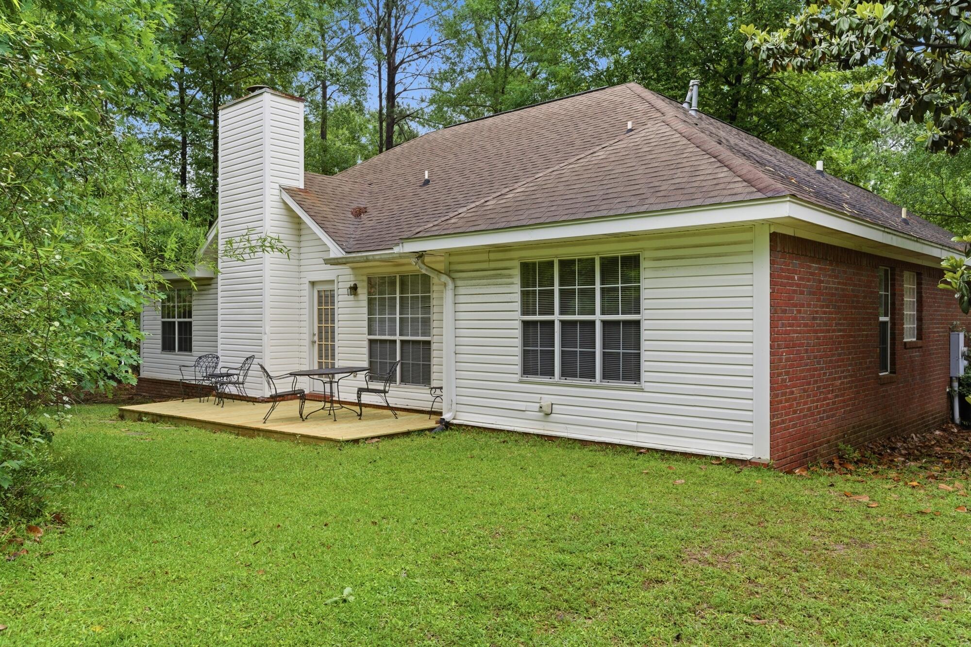 House rear exterior with a wooden patio deck, metal furniture, and a tree-lined lawn.
