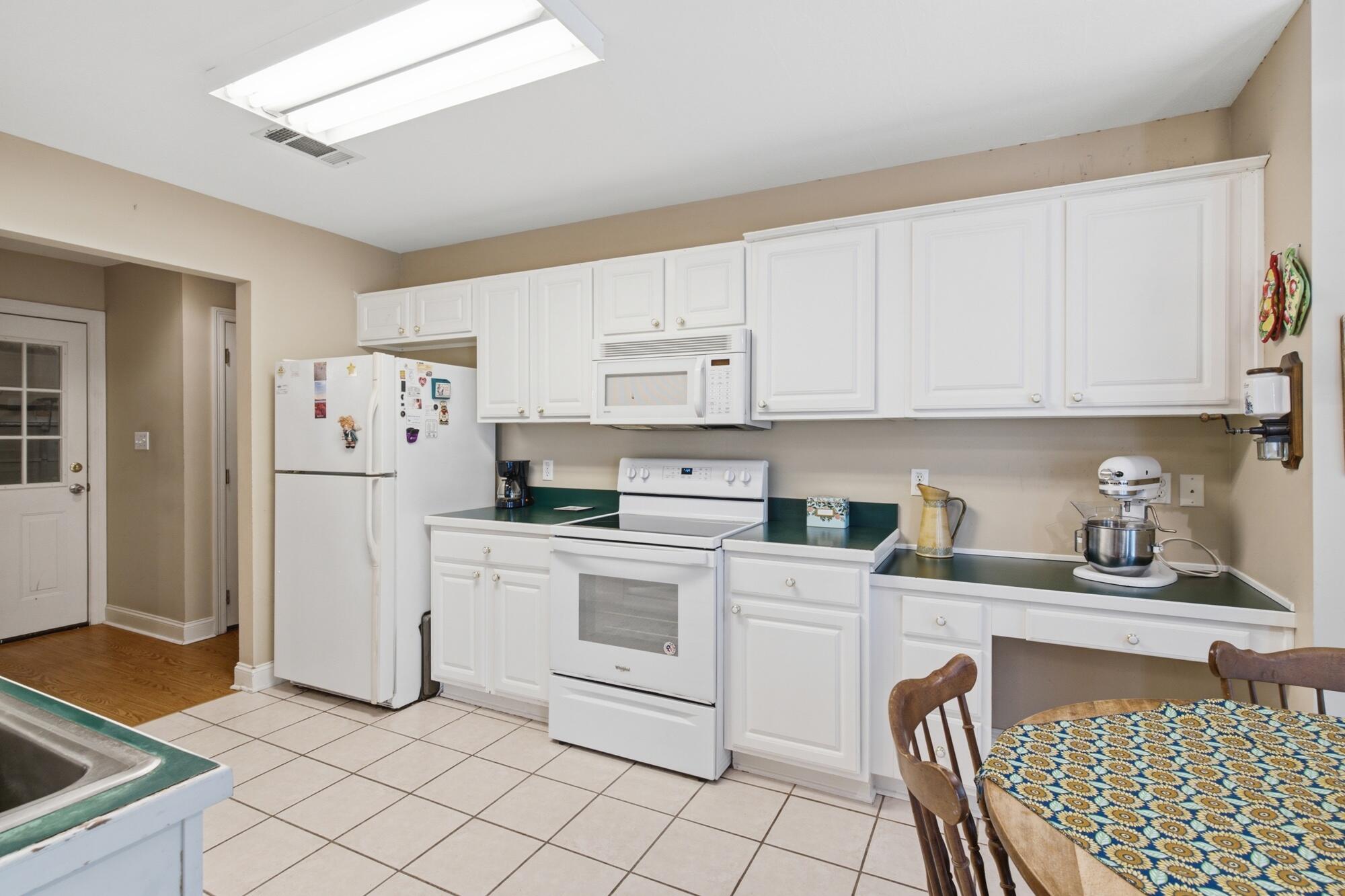 Kitchen with white cabinets, dark green countertops, white appliances, and a patterned dining table.