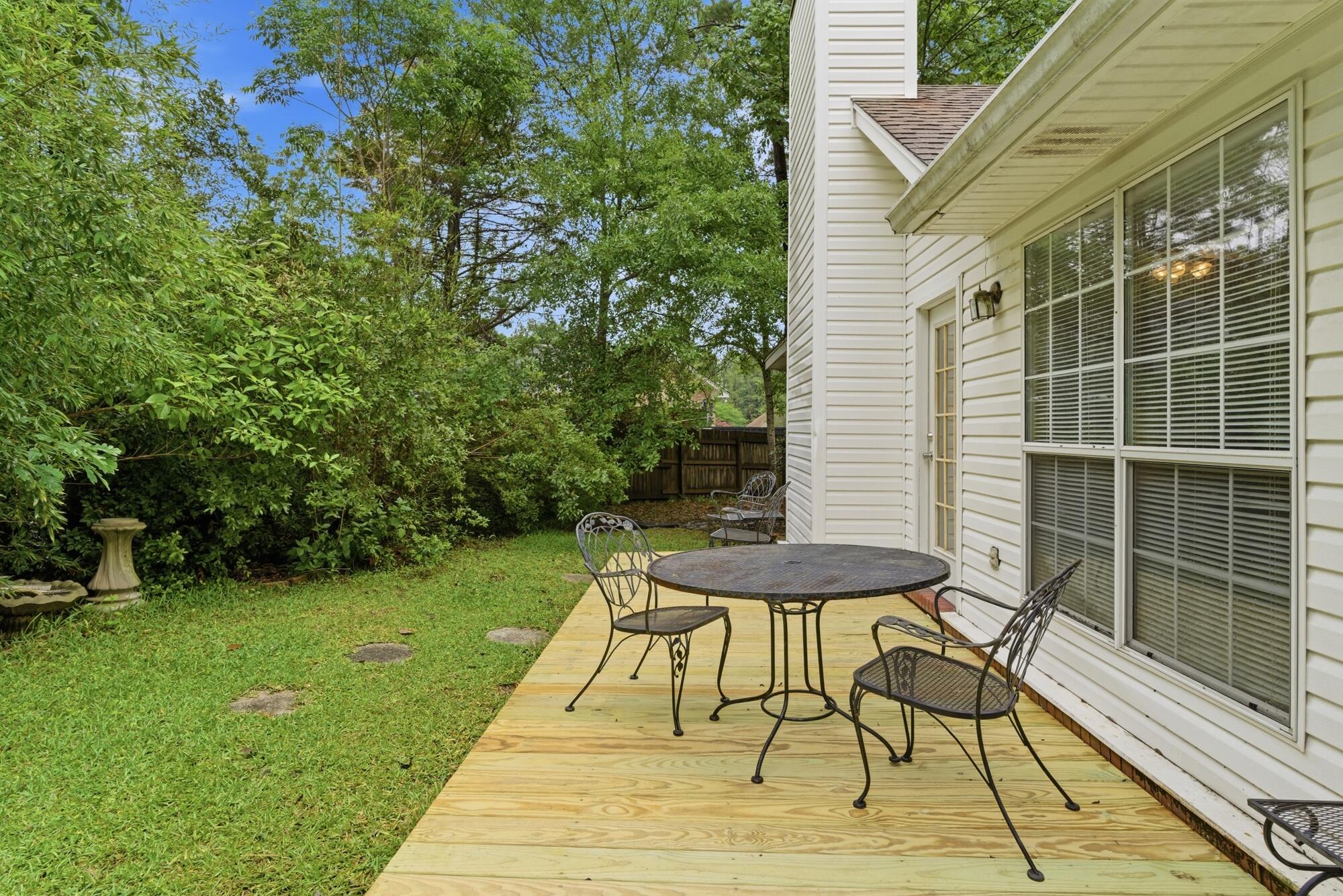 Wooden backyard deck with a round patio table and chairs beside a white-sided house.