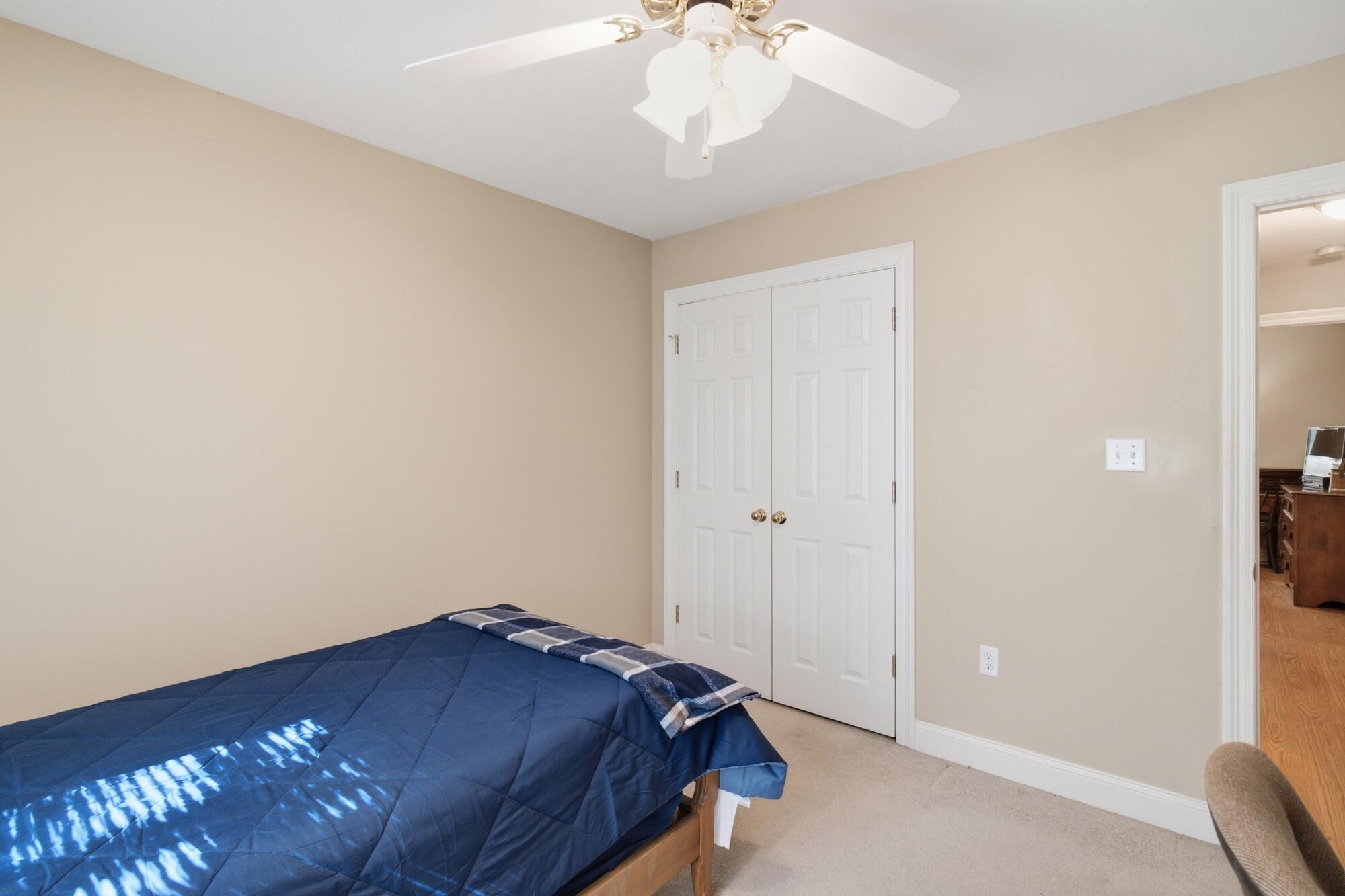 Bedroom with a blue-covered bed, white closet doors, and a ceiling fan.