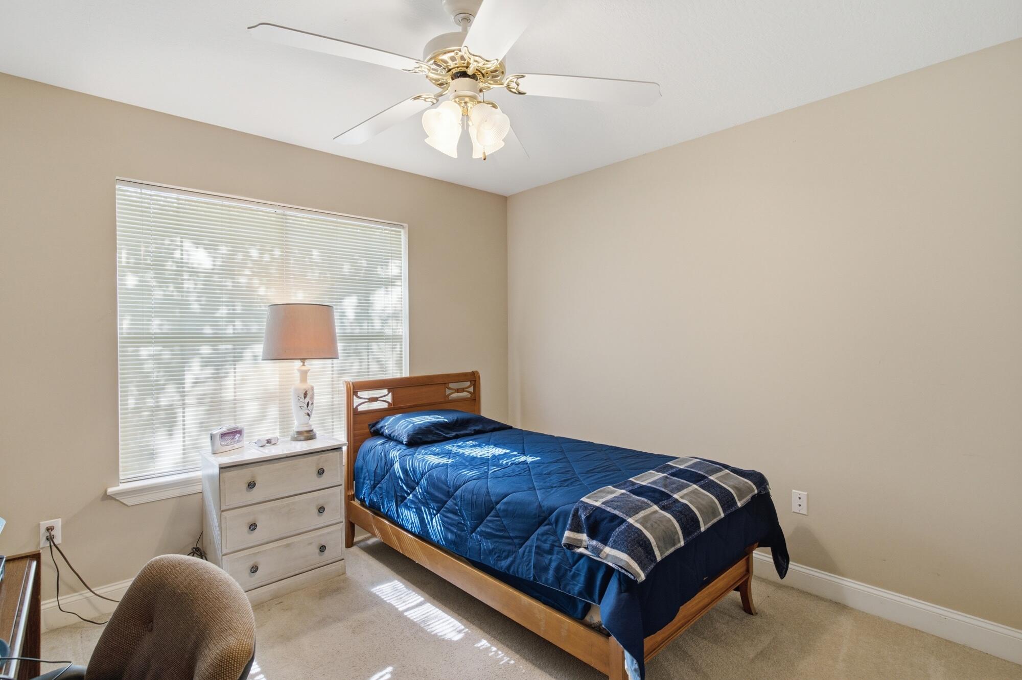 Bedroom with a wooden bed in blue bedding, plaid throw, and a large window with blinds.