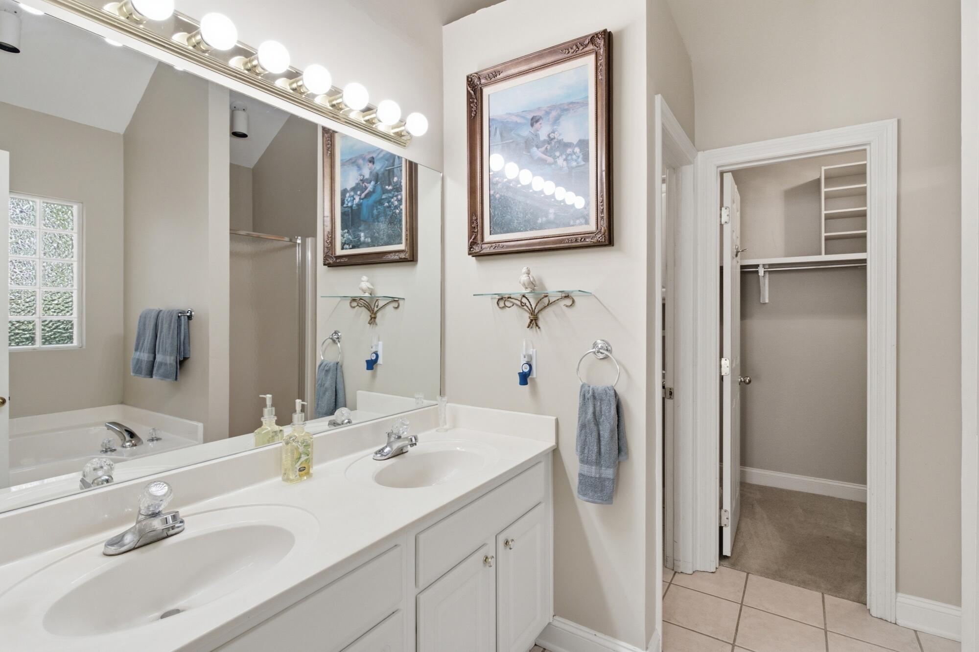 Bathroom with a double-sink vanity, large mirrors, glass-block window, and open closet.