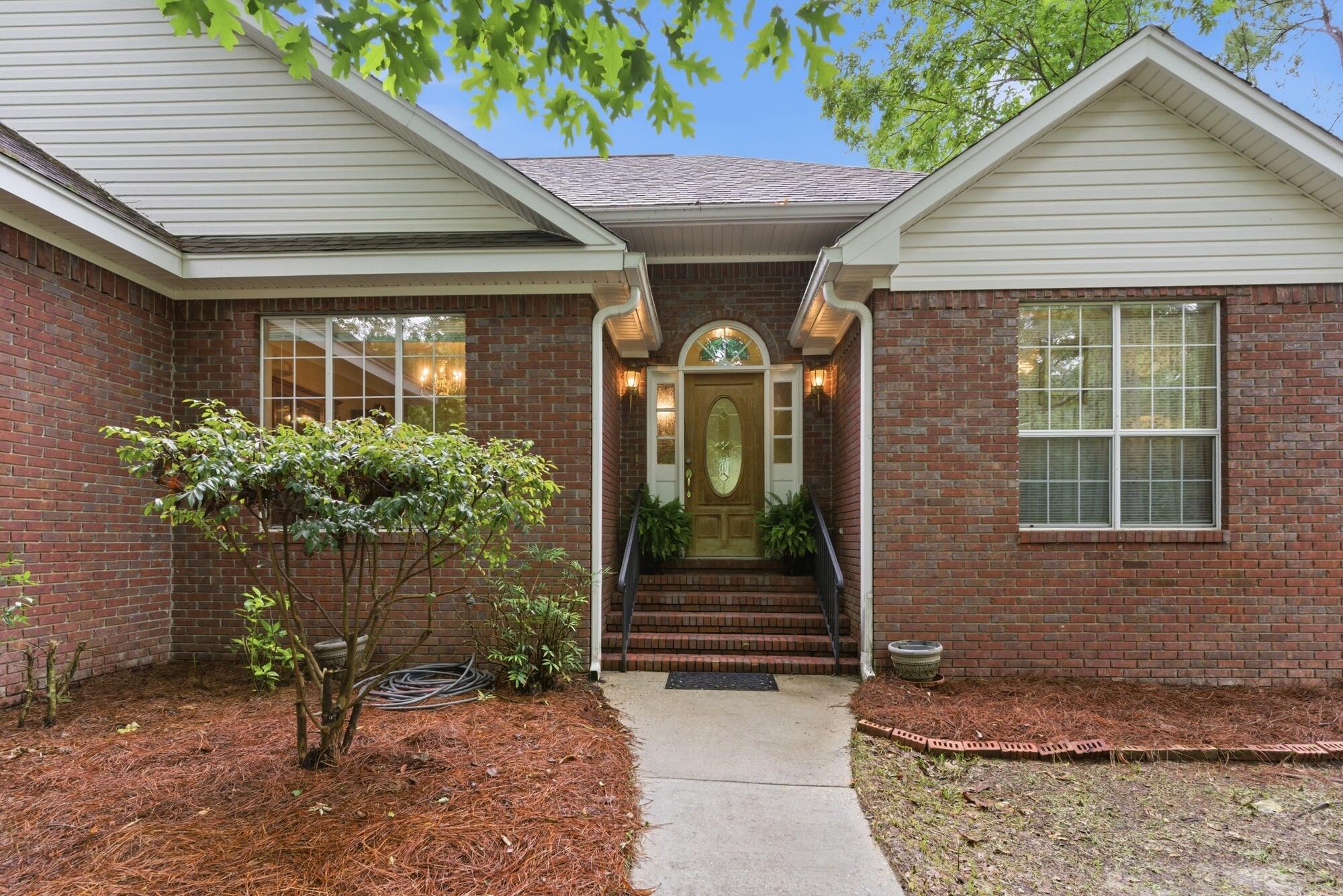 Red-brick home with white gables, a recessed front entrance, brick steps, and landscaped foundation.