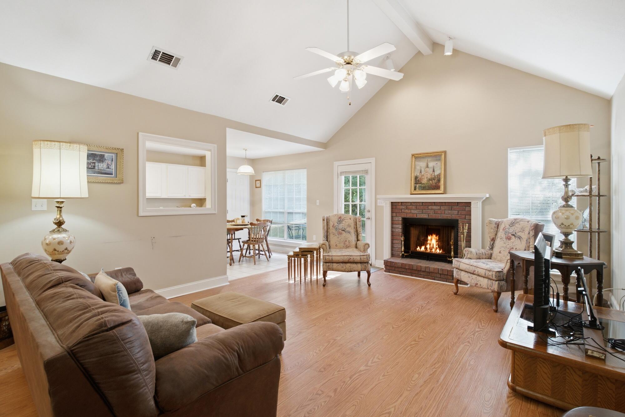 Living room with a vaulted ceiling, lit brick fireplace, and hardwood floors.