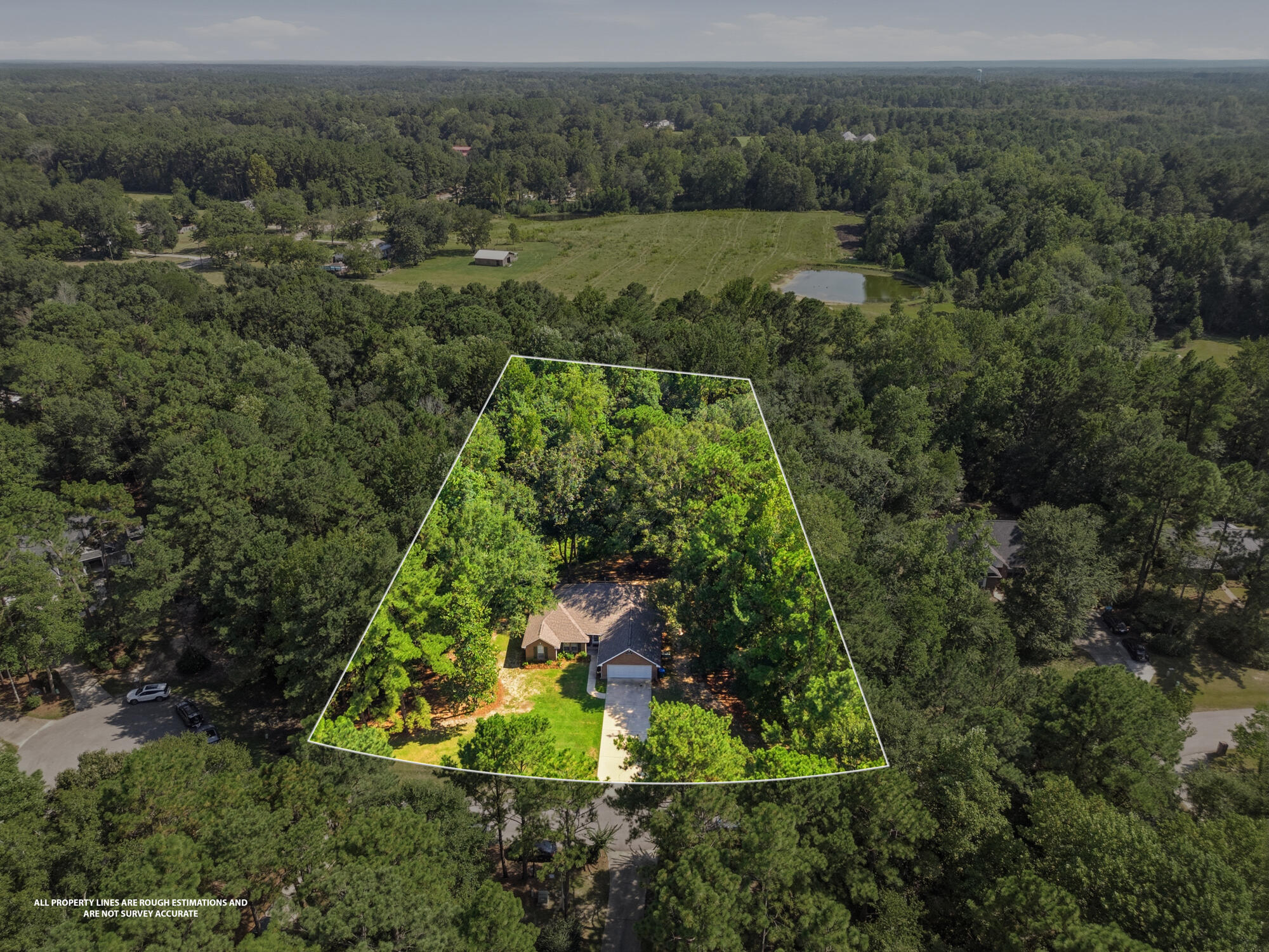 Aerial view of a house and driveway within a white-outlined, wooded property boundary.