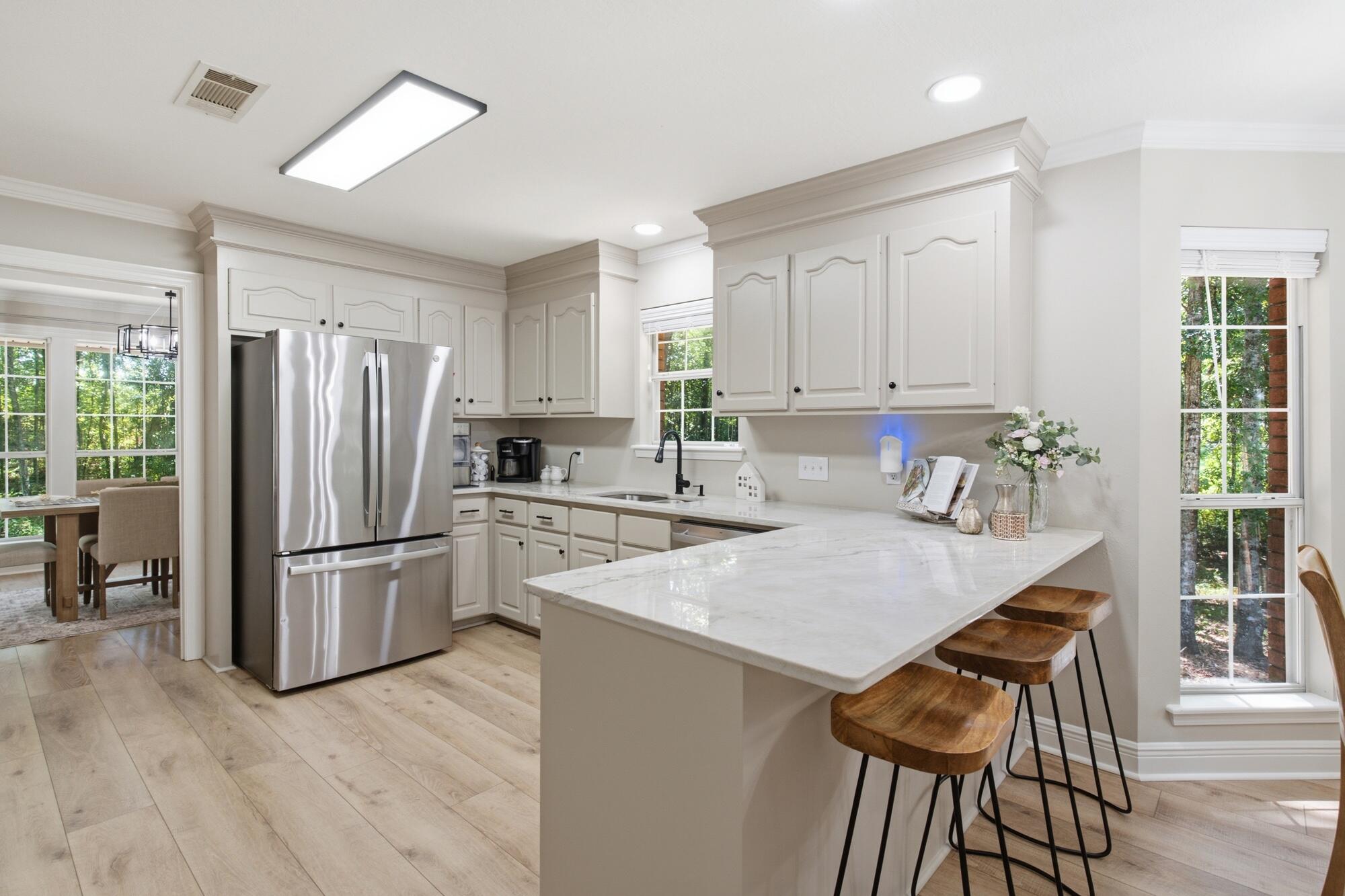 Bright kitchen with white cabinets, stainless steel refrigerator, and a large island with wooden stools.