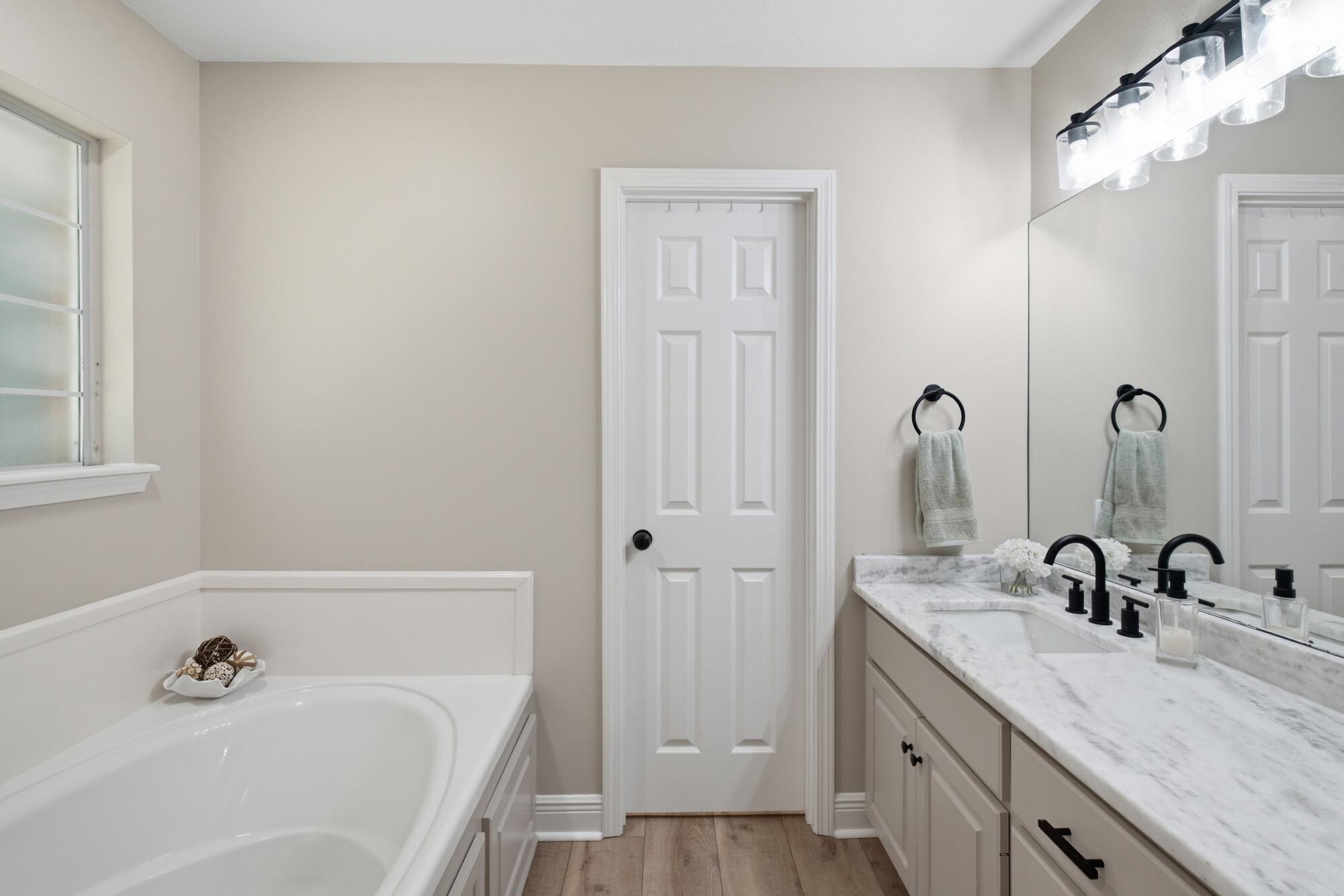 Bathroom with a soaking tub, marble-look vanity, black fixtures, and a large mirror.
