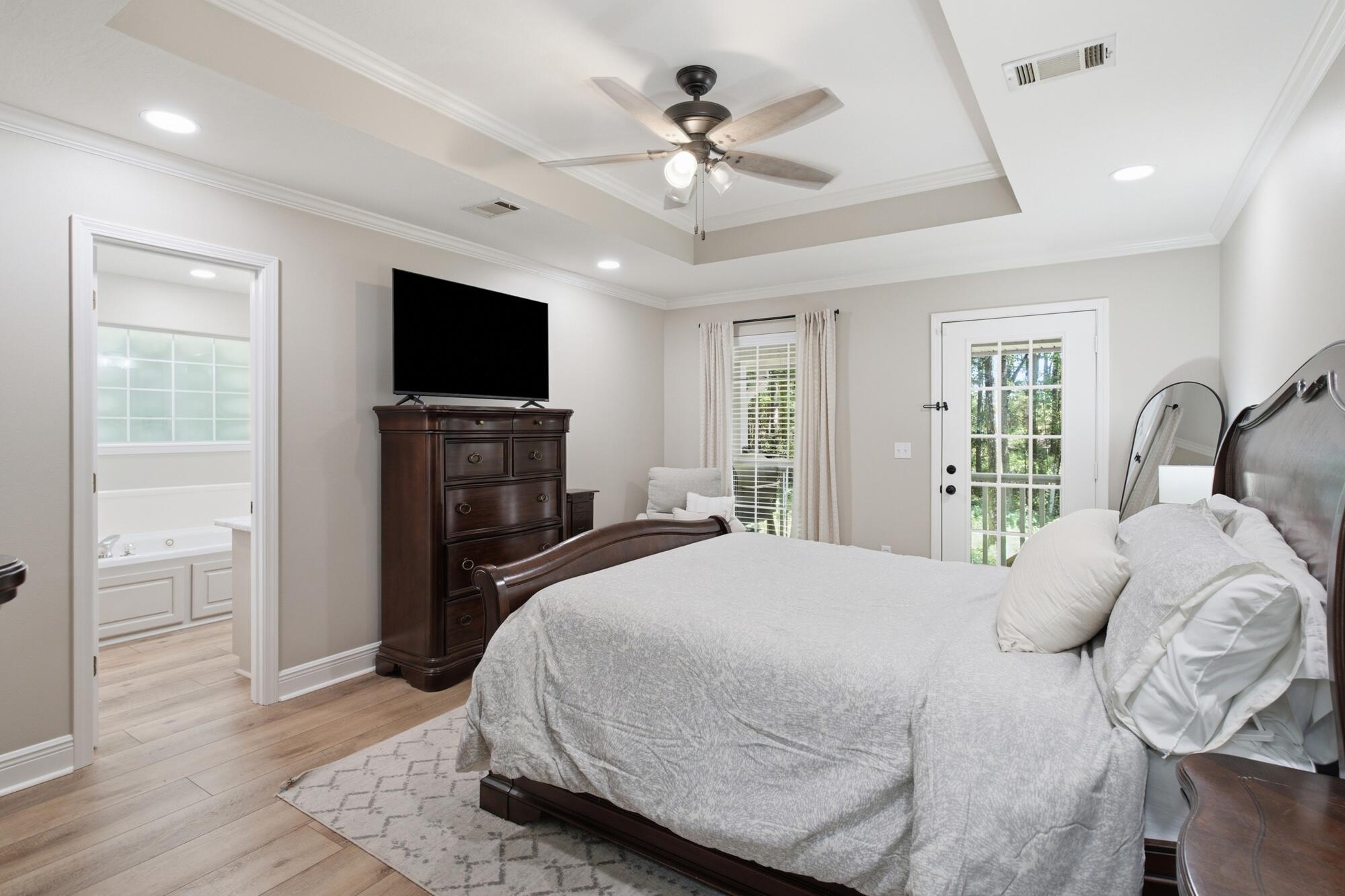 Furnished bedroom with a dark wood bed, tray ceiling, and doorway to an en suite bathroom.