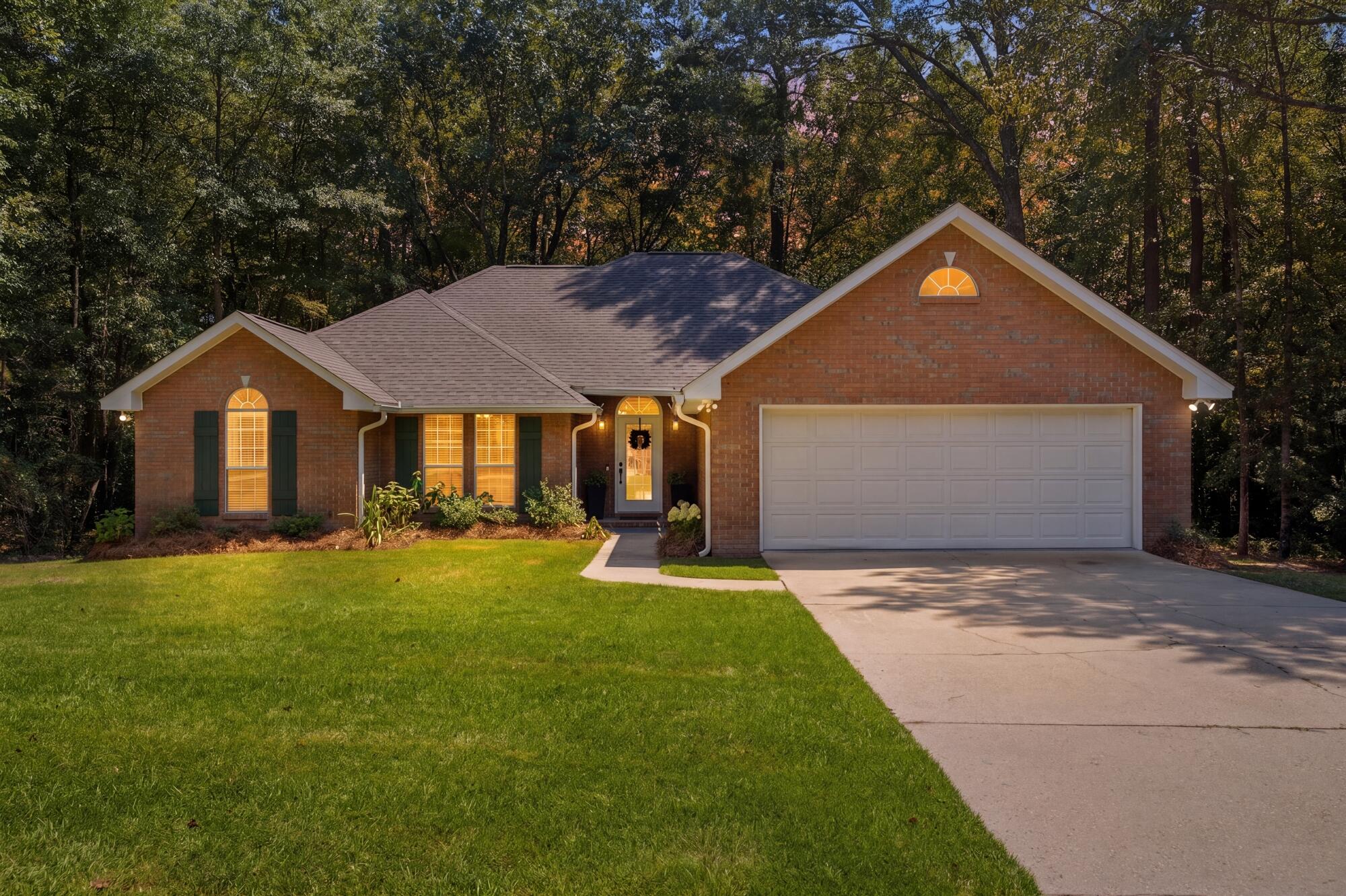 Red-brick home with arched windows, a two-car garage, and a lawn bordered by mature trees.