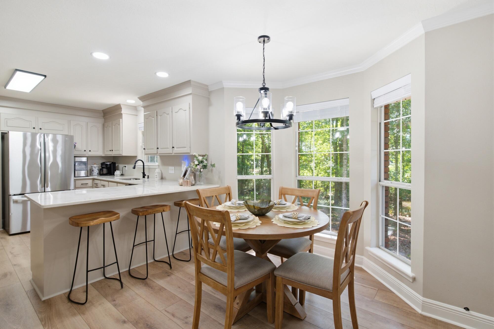 Bright kitchen and dining area with a quartz breakfast bar and a round table beside tall windows.