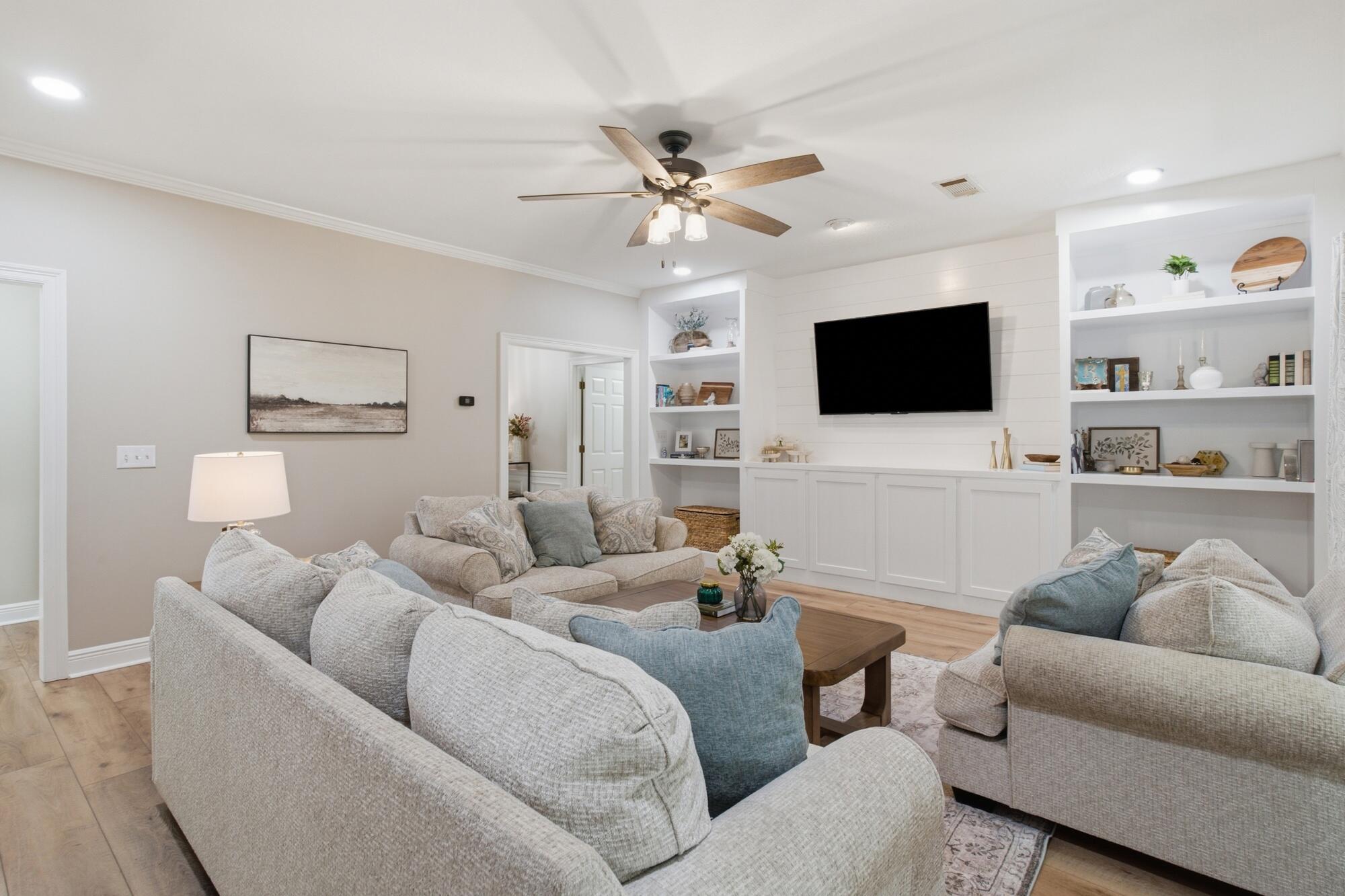 Living room with neutral sofas, a wood coffee table, and a wall-mounted TV framed by built-in shelves.