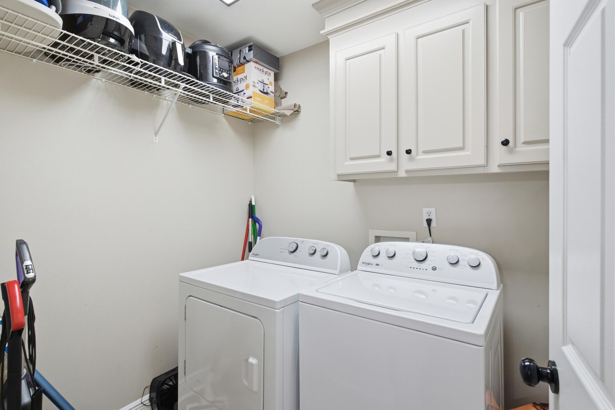 Laundry room with white washer and dryer, upper cabinets, and wire shelving.