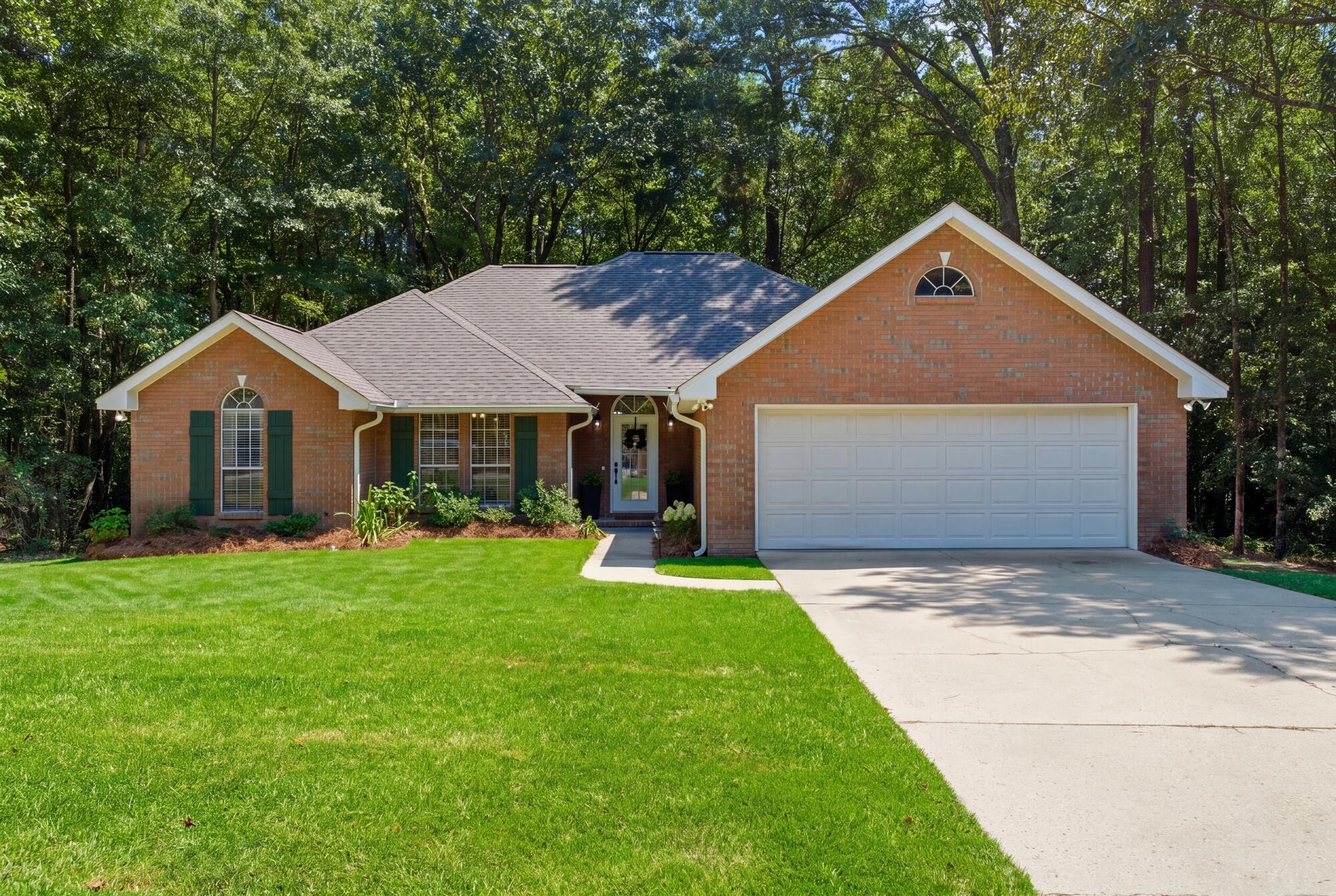 Red-brick home with a two-car garage, green lawn, and mature trees.