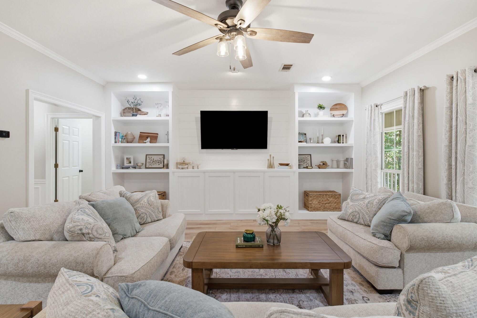 Living room with light sofas, a wood coffee table, and built-in shelving around a wall-mounted television.