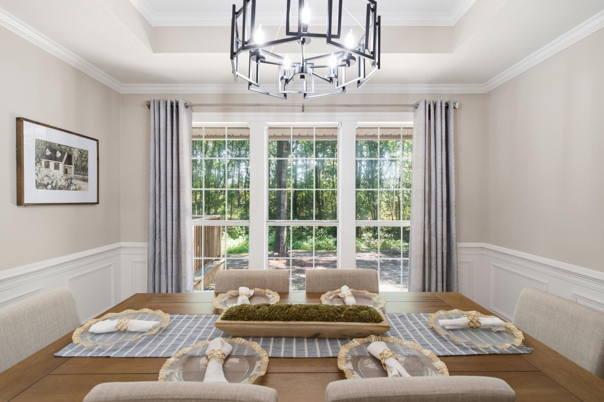 Dining room with a table set for six and large windows overlooking trees.