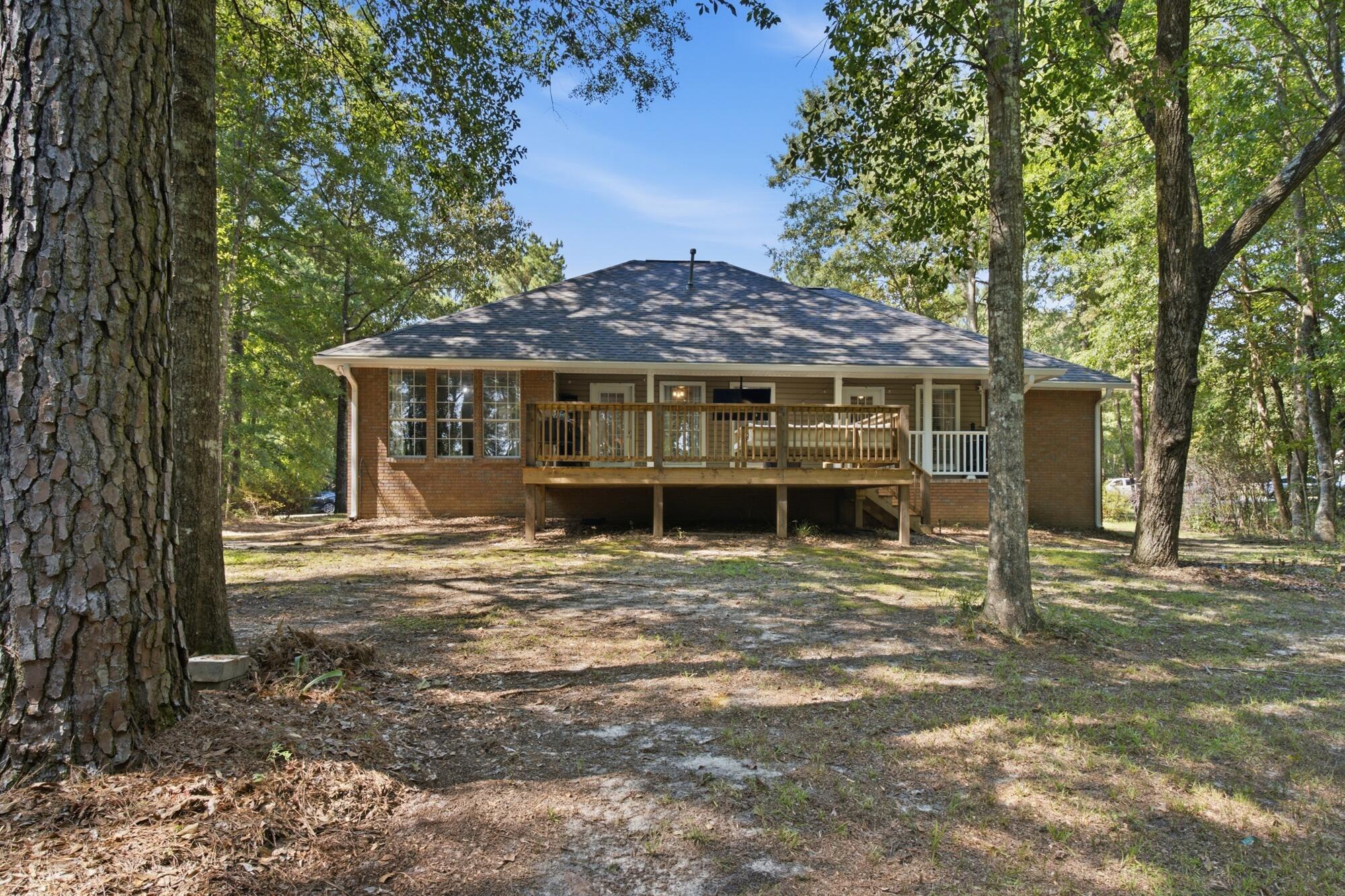 Home’s rear exterior with an elevated wooden deck among mature trees.