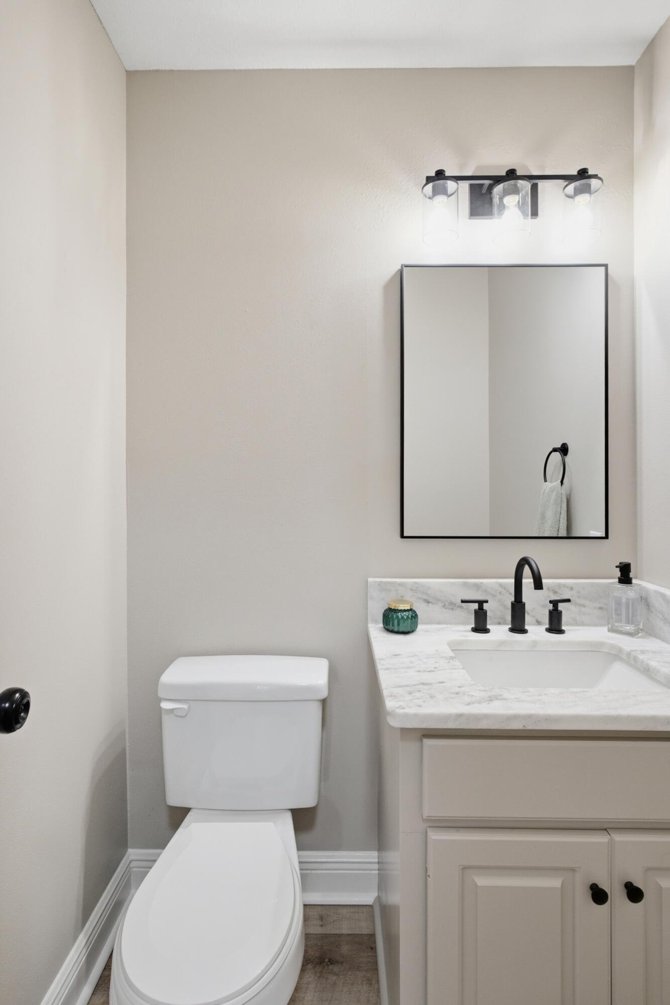 Bathroom with a white toilet, marble-look vanity, black fixtures, and a rectangular mirror.