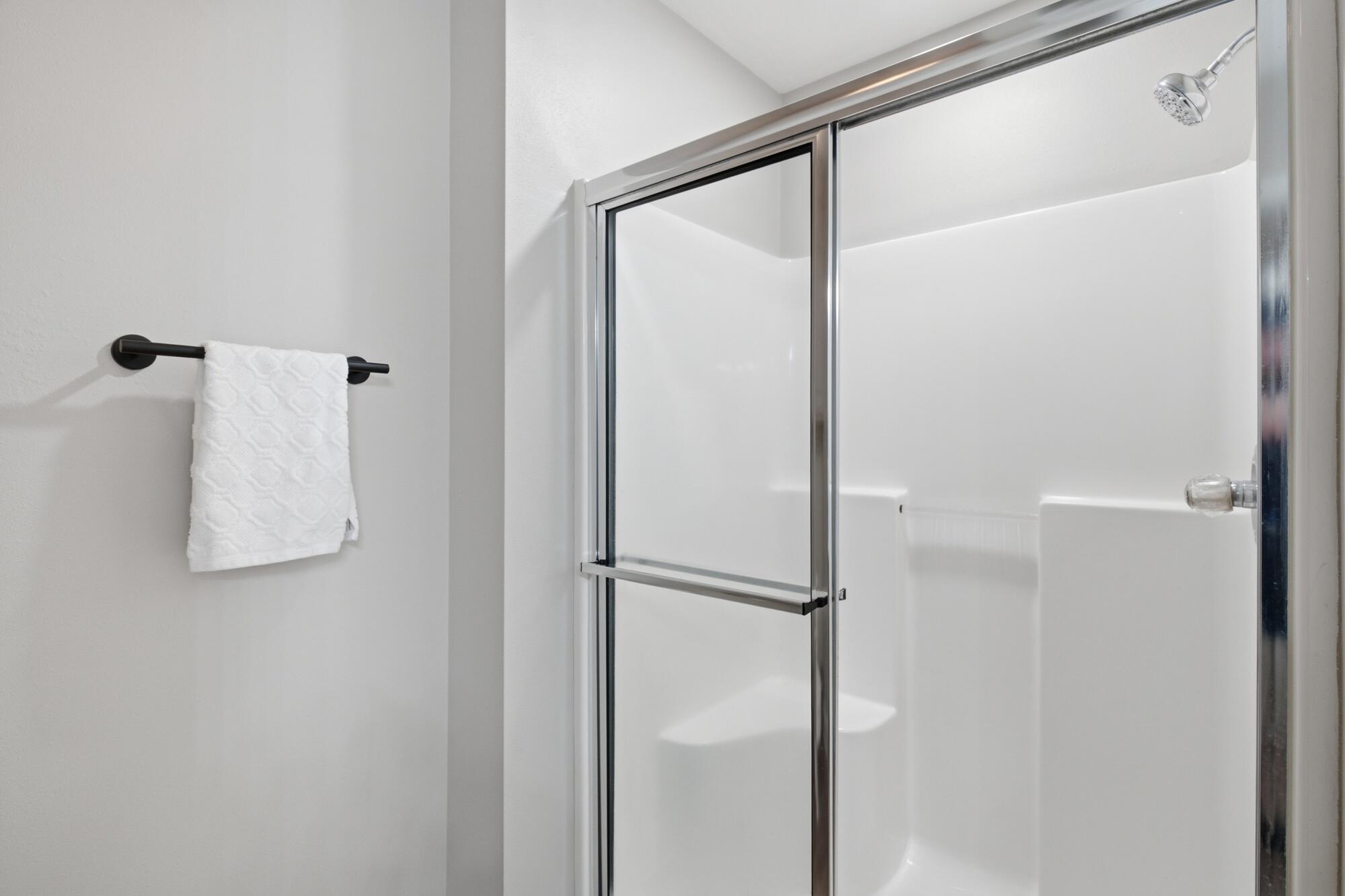 Bathroom shower with glass doors and chrome trim beside a white towel on a black bar.