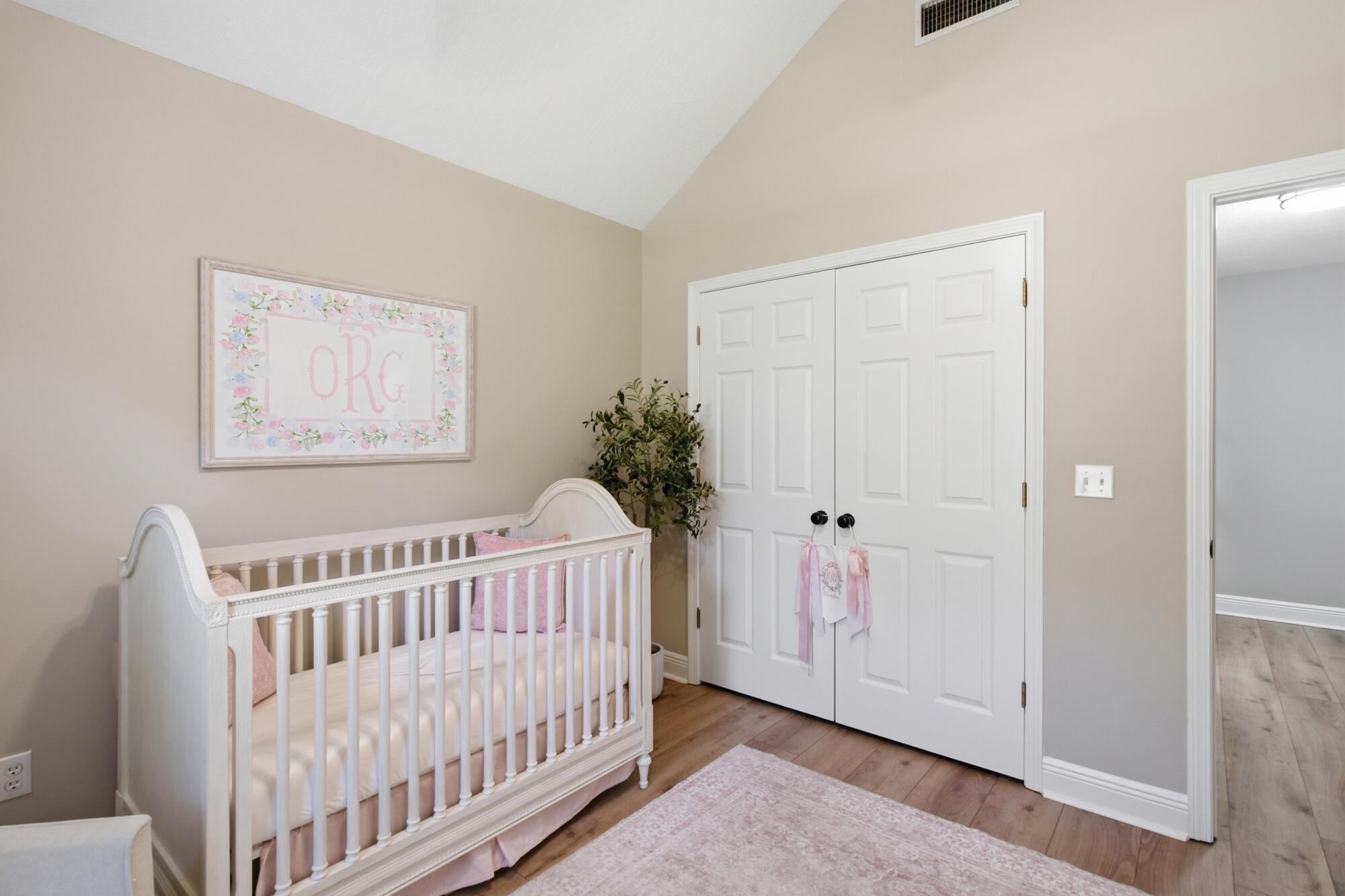 Nursery with a white crib, pink bedding, floral wall art, and white closet doors.