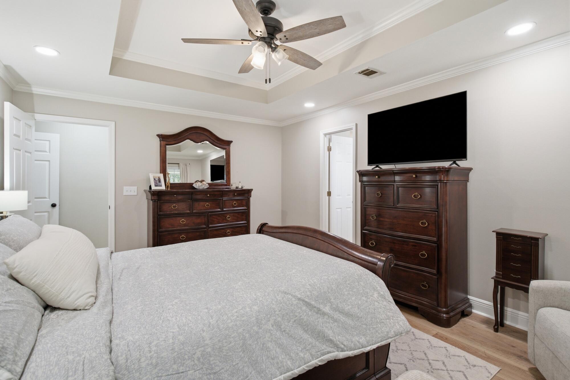 Bedroom with a tray ceiling, ceiling fan, large bed, dark wood furniture, and wall-mounted television.