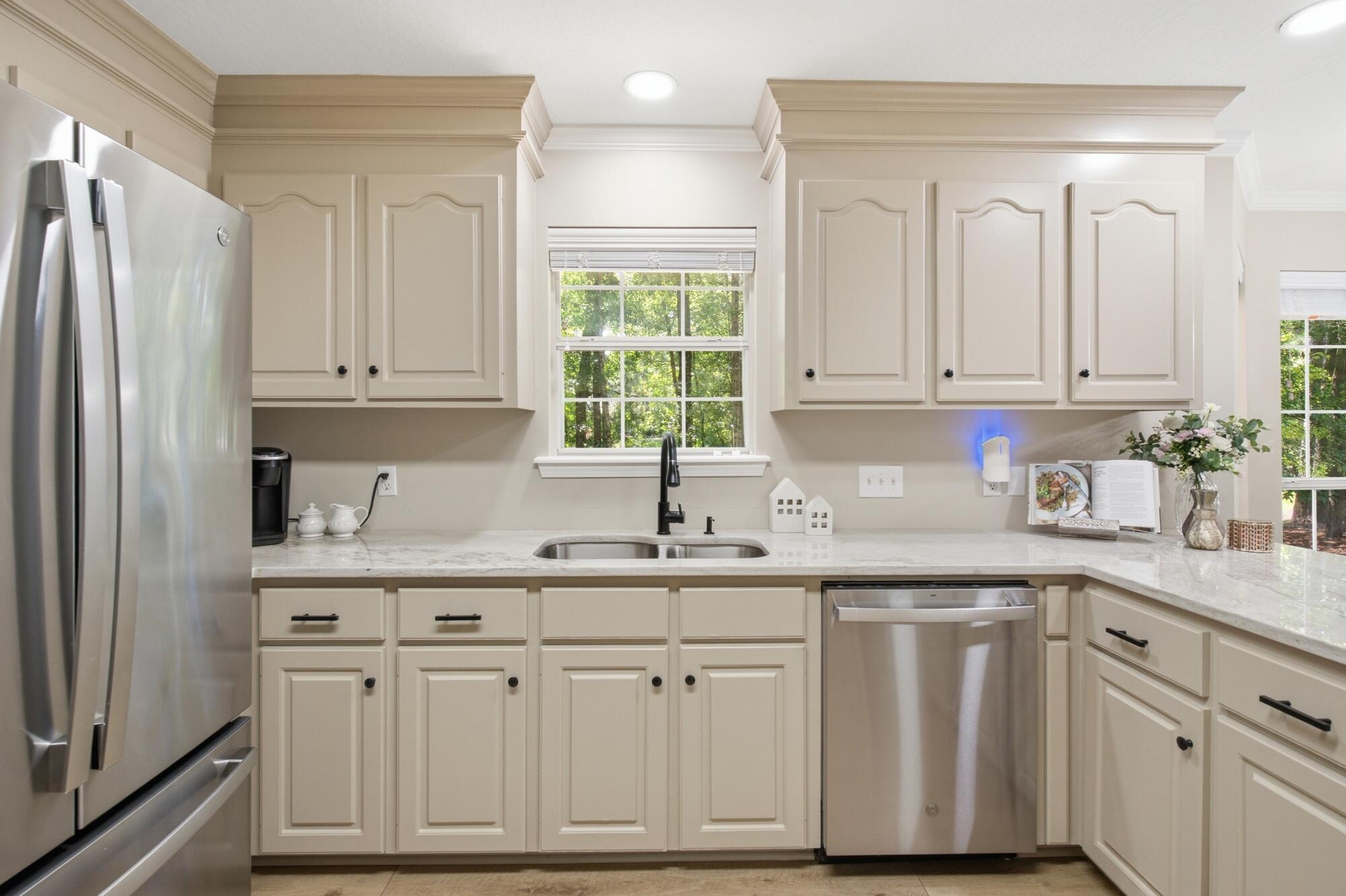 Bright kitchen with cream cabinets, stone counters, stainless appliances, and a sink beneath a window.