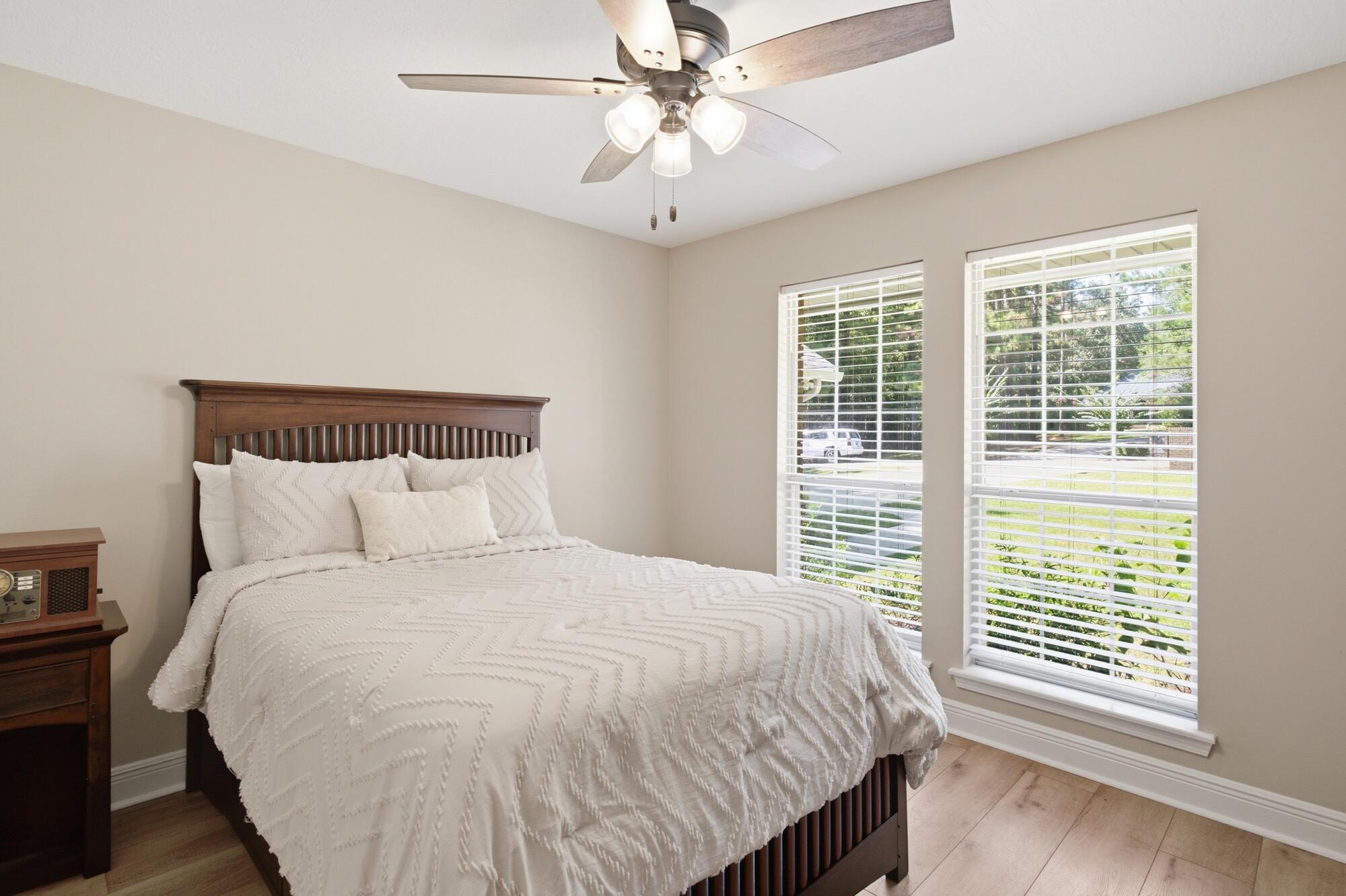 Bedroom with a dark wood bed, white bedding, and two large windows with blinds.
