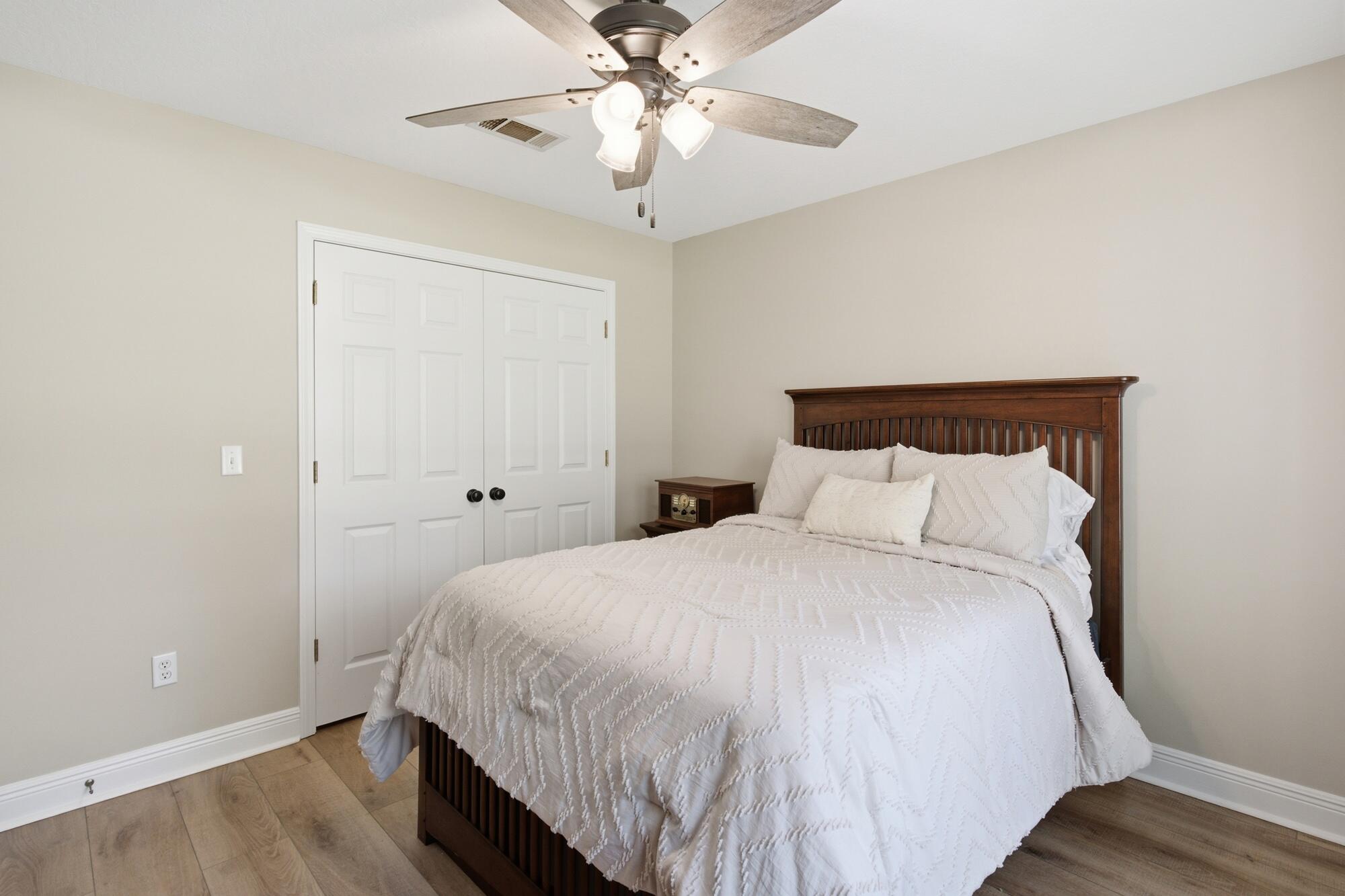 Bedroom with a dark wood bed, white quilted bedding, double closet doors, and a ceiling fan.