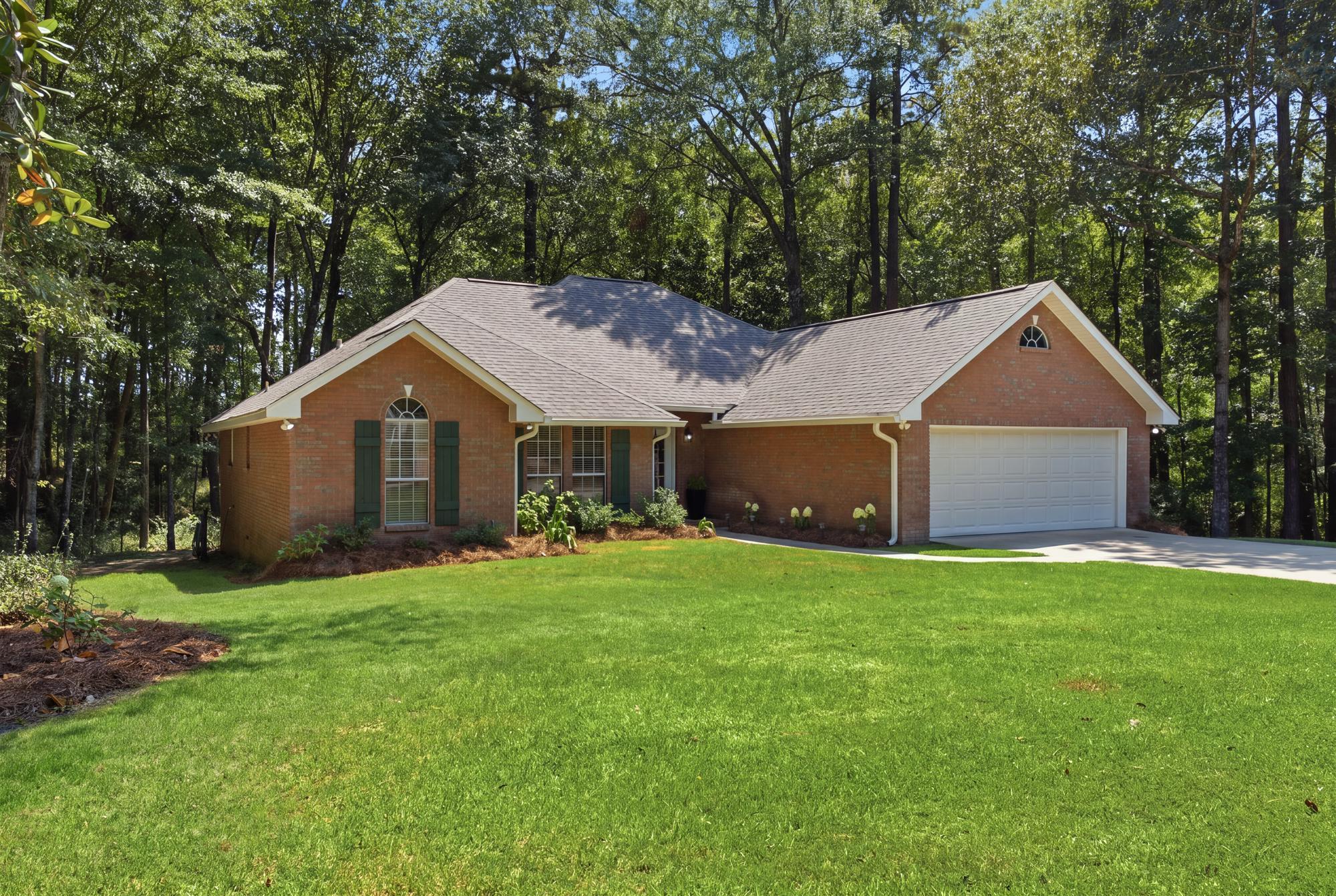 Red brick home with a white garage, broad green lawn, and mature trees.