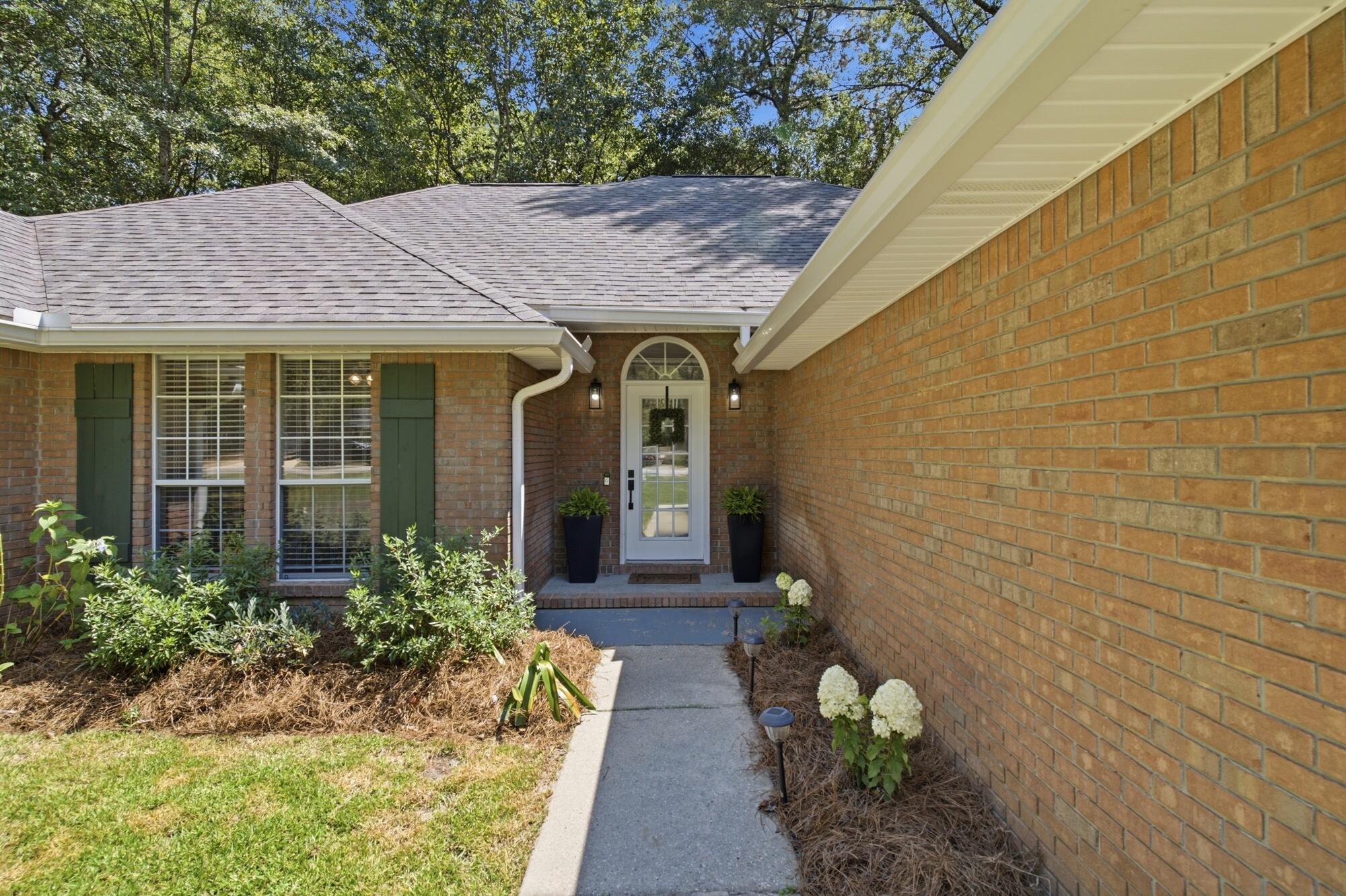 Brick home entrance with a recessed white glass-paneled door, green shutters, and landscaped walkway.