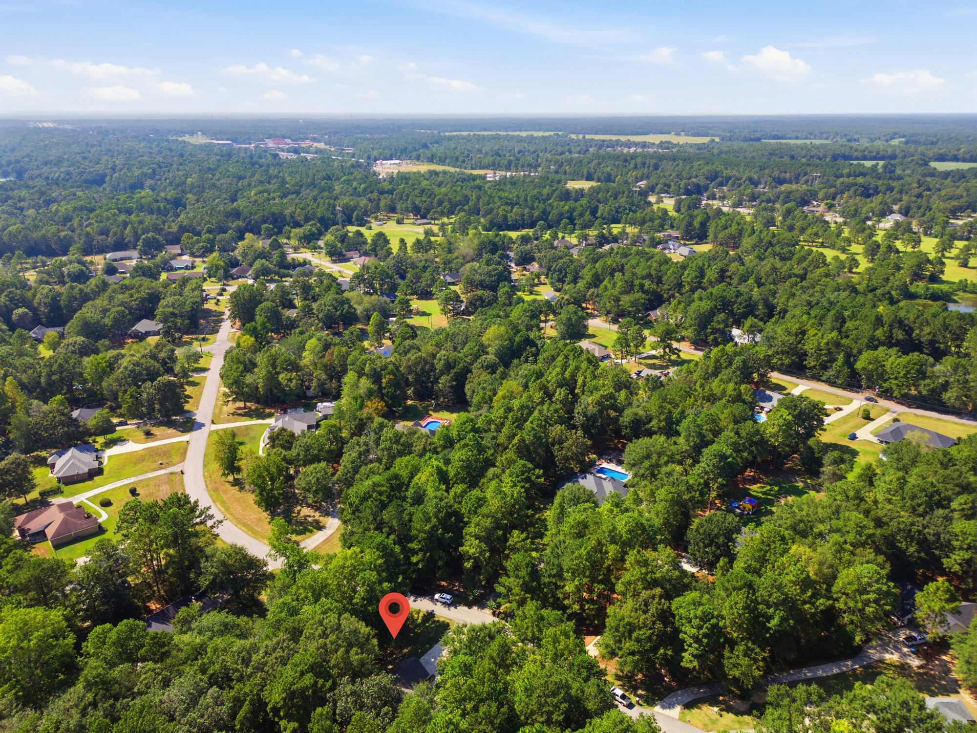 Aerial view of a wooded neighborhood, with a red map pin marking a home along a residential street.