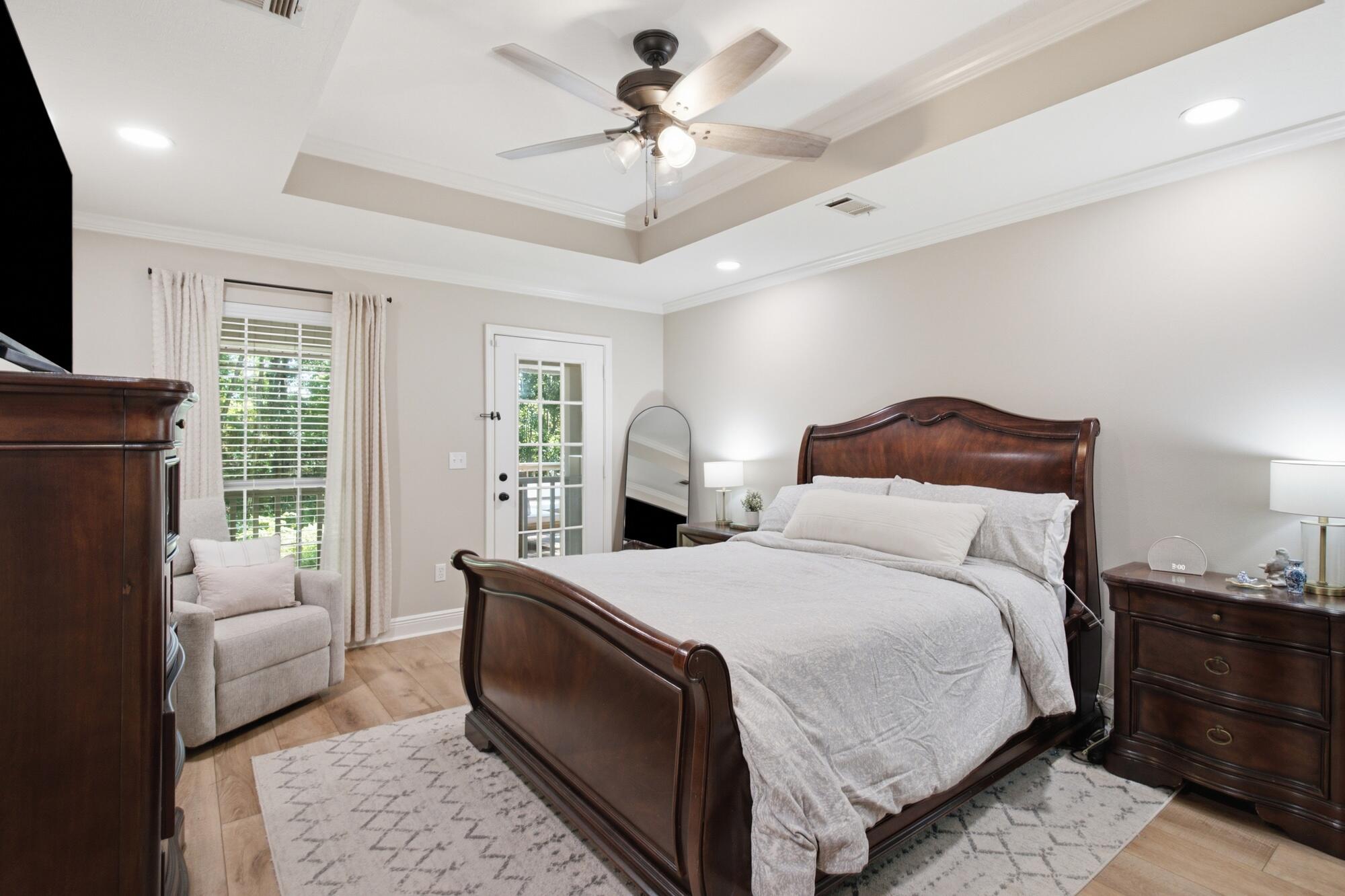 Furnished bedroom with a dark wood bed, tray ceiling, and ceiling fan.