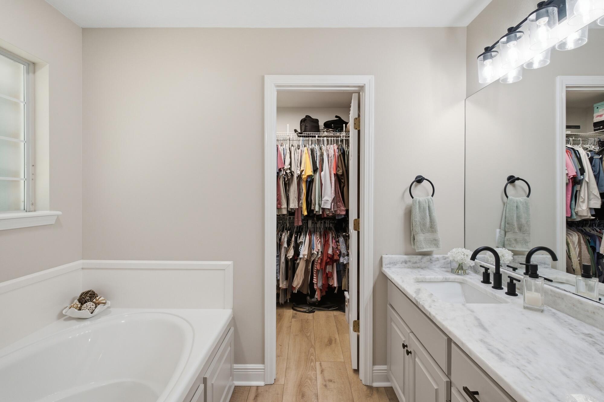 Bathroom with a soaking tub and marble double vanity, opening to a walk-in closet.