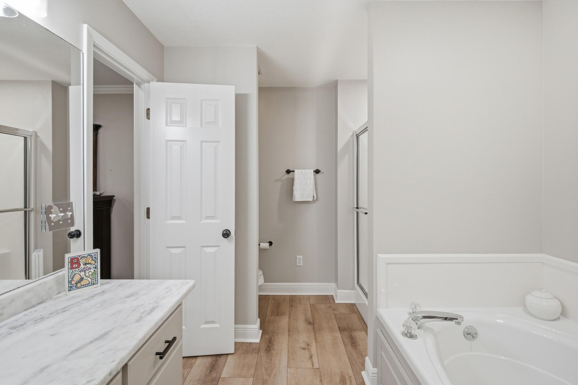 Bathroom with a white soaking tub, glass shower, and marble-look vanity countertop.