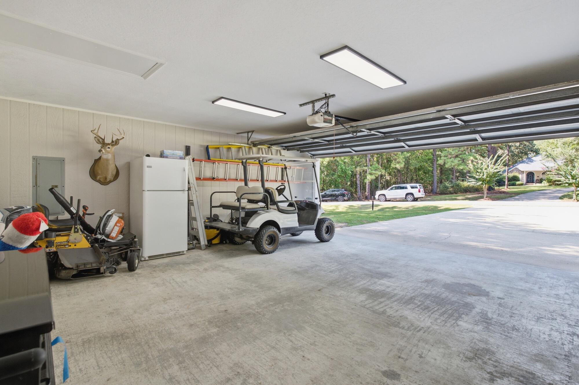 Open garage with a golf cart, lawn mower, refrigerator, and ladders.