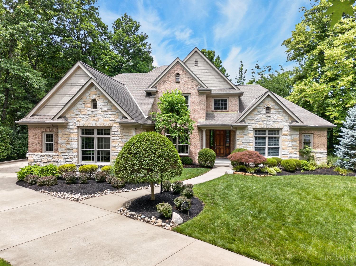 Stone-and-brick home with multiple gabled roofs, landscaped lawn, and a curving front walkway.