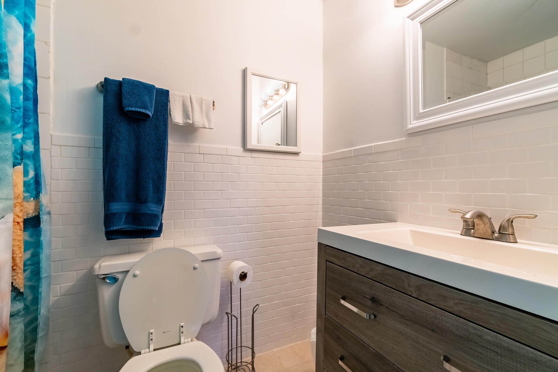 Bathroom with white subway tile, dark wood vanity, and blue patterned shower curtain.