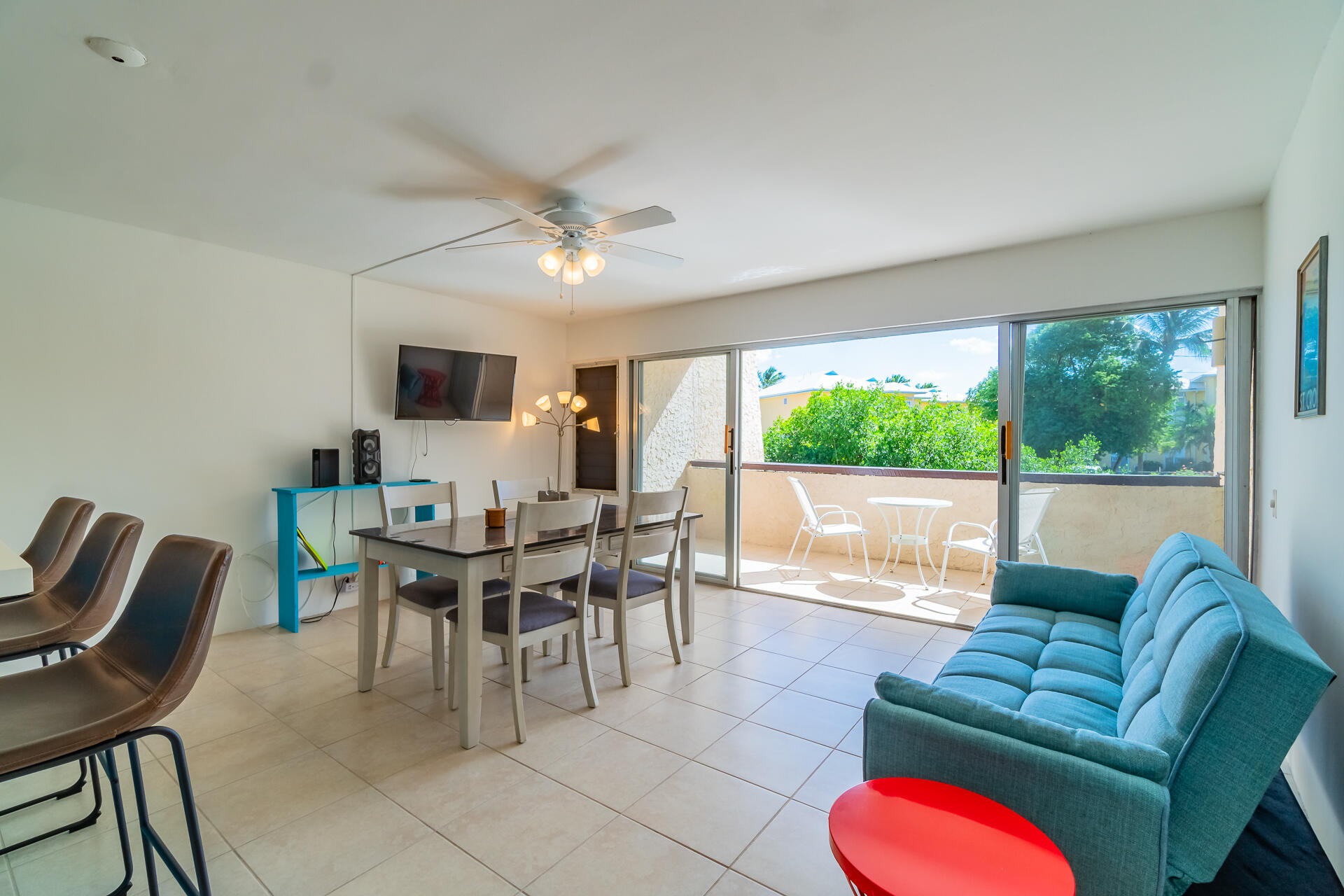Living and dining area with turquoise sofa and sliding doors opening onto a sunny patio.