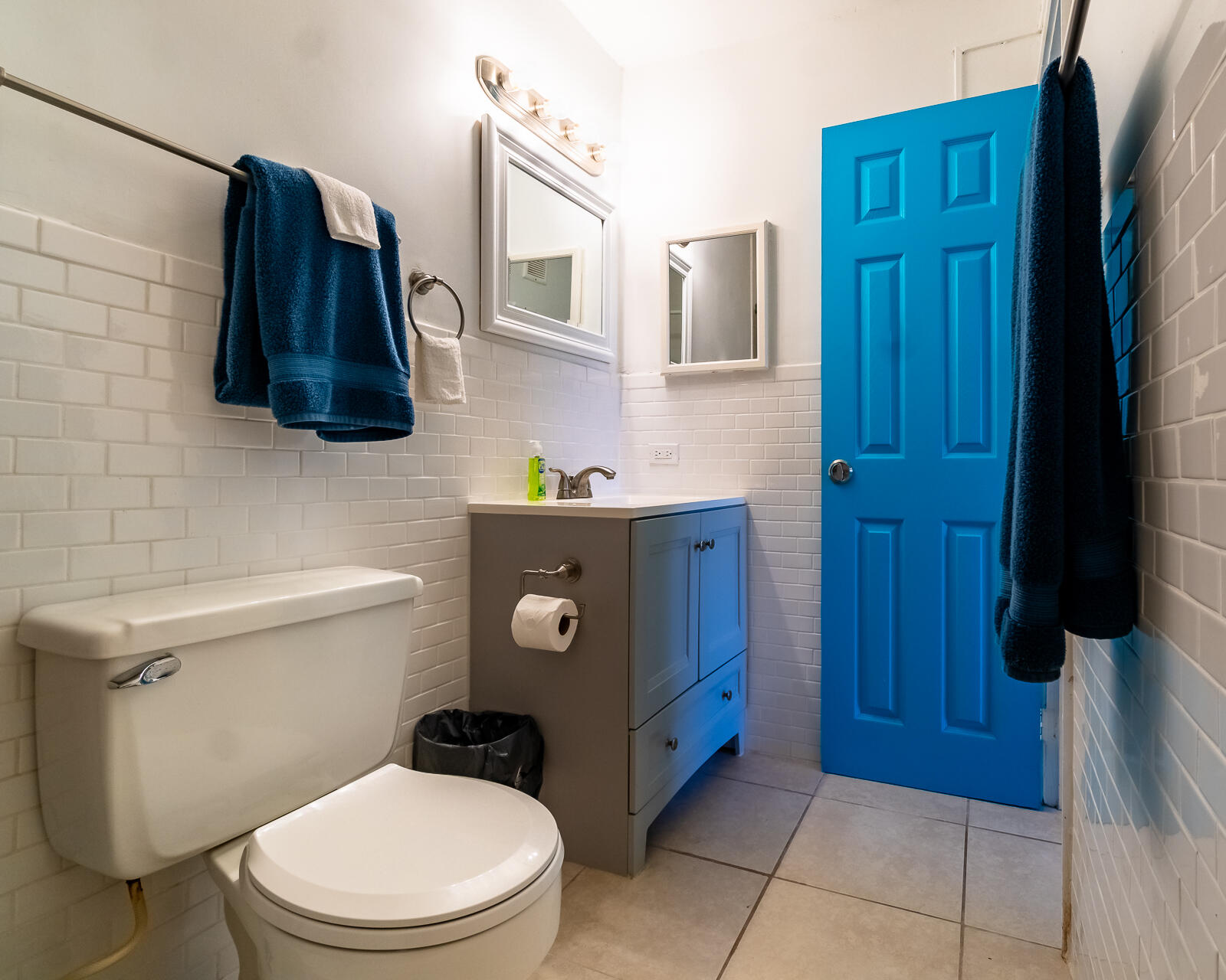 Bathroom with a gray vanity, white subway tile, and a bright blue door.