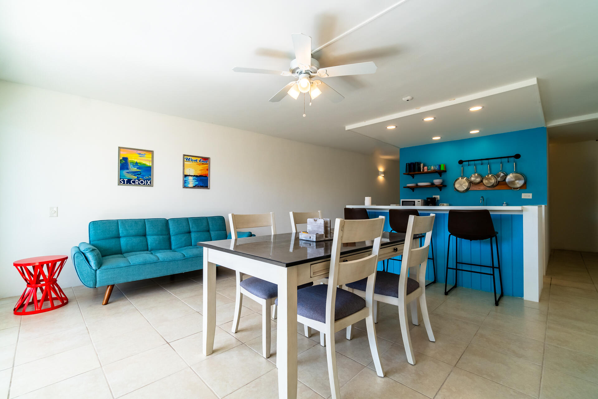 Open-plan dining area with a white table, turquoise sofa, and blue kitchen island.