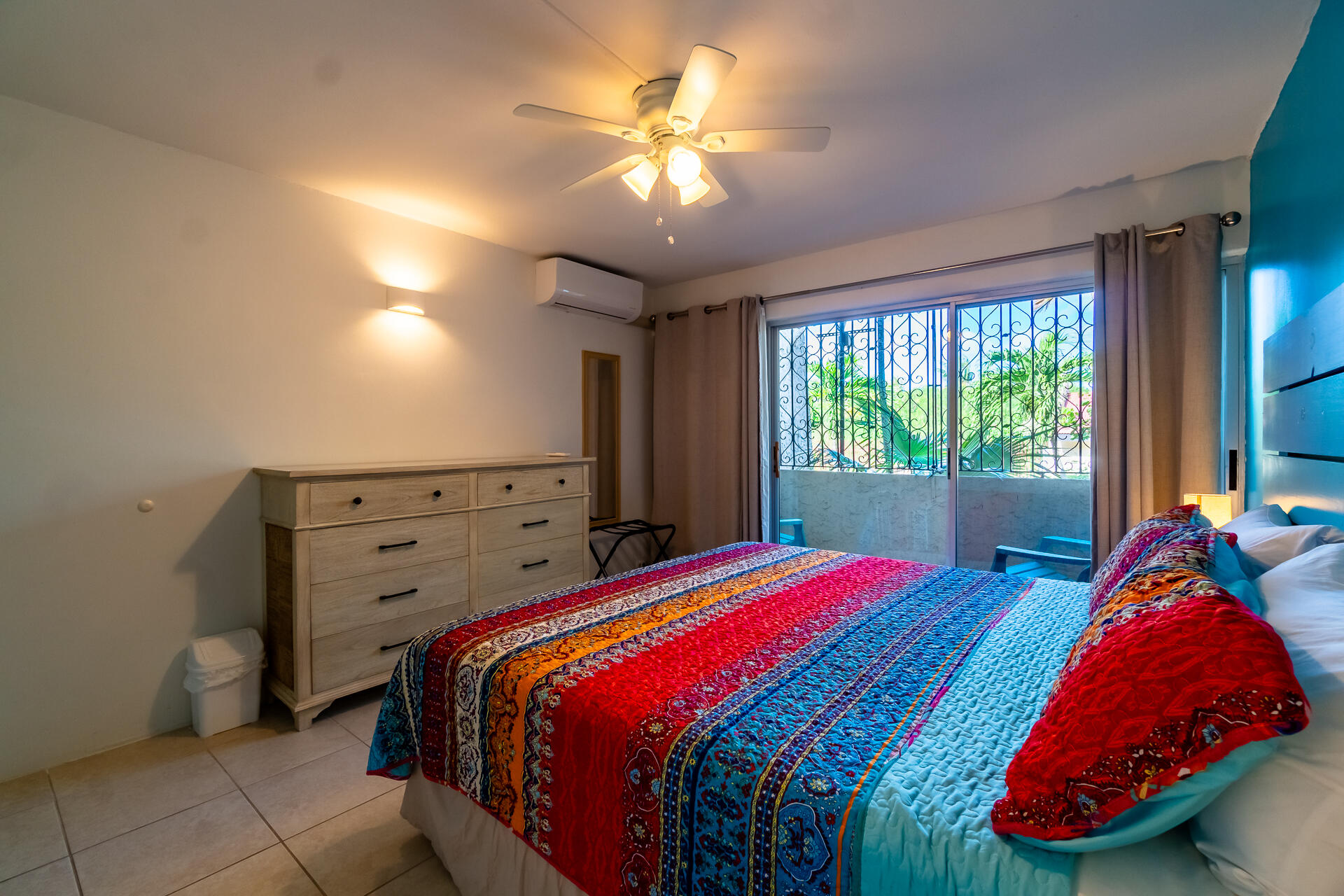 Furnished bedroom with a colorful quilted bed and sliding glass doors overlooking greenery.