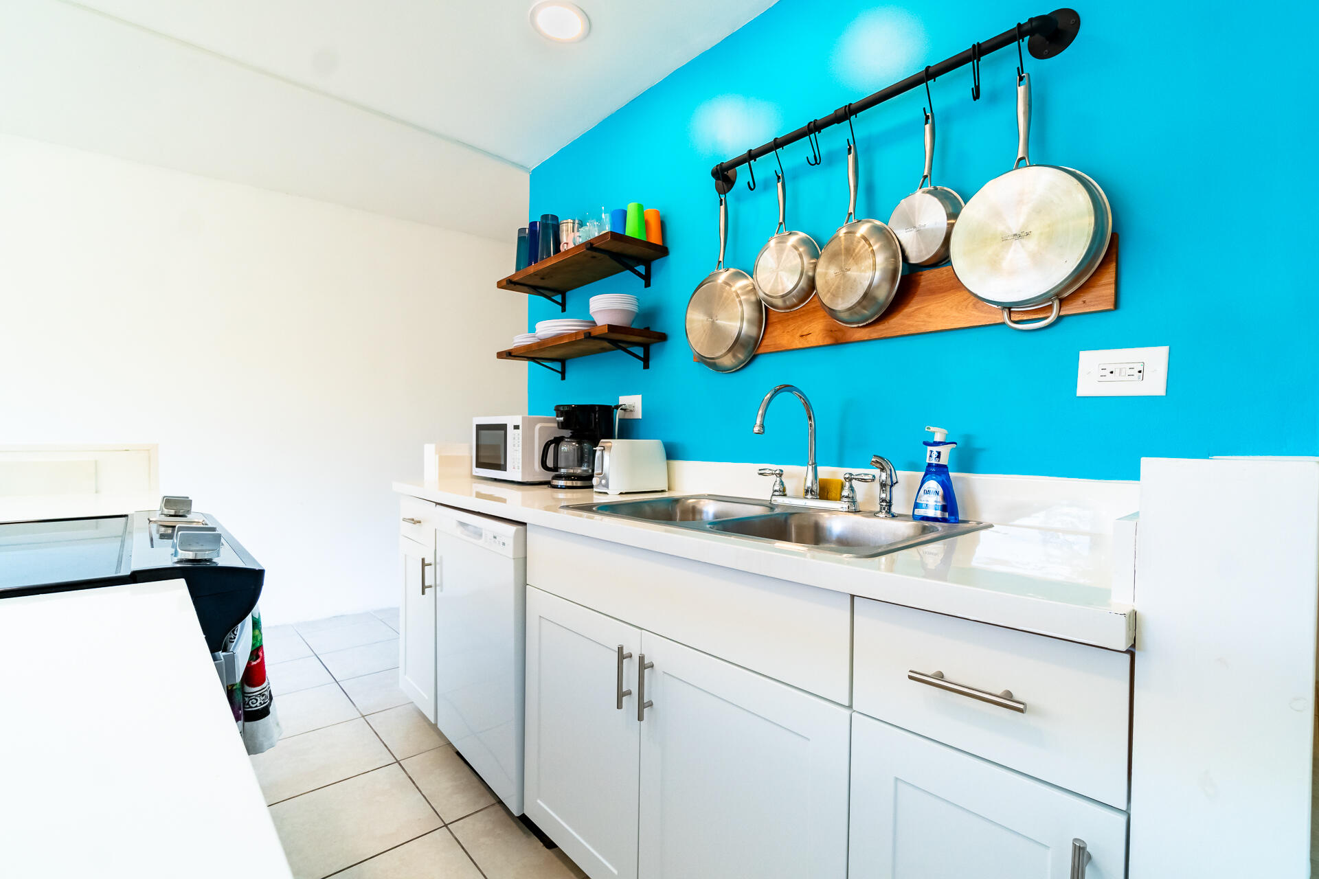 Kitchen with a double sink, hanging cookware, and a vivid turquoise accent wall.