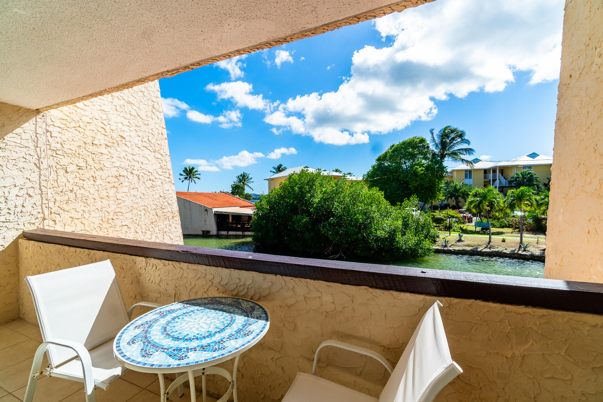 Covered balcony with a blue mosaic table overlooking a waterway and tropical landscaping.