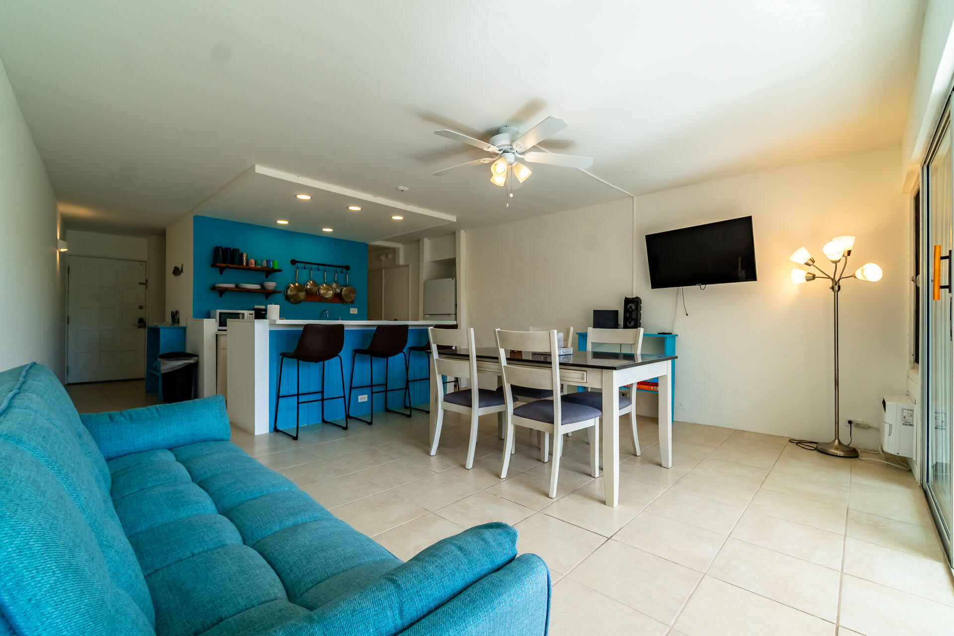 Open-plan living and dining area with a turquoise sectional, white dining set, and bright blue kitchen island.