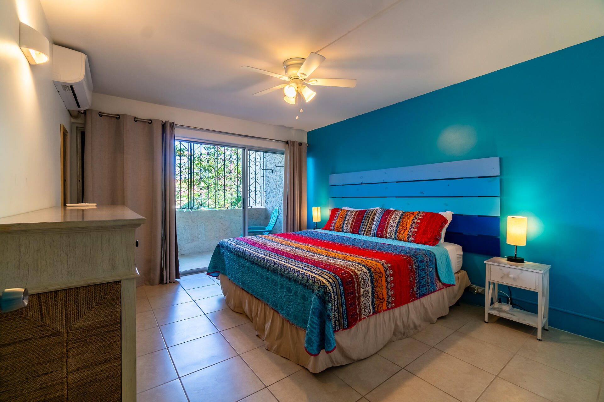 Bedroom with a colorful patterned bedspread, turquoise accent wall, and sliding glass door to a balcony.