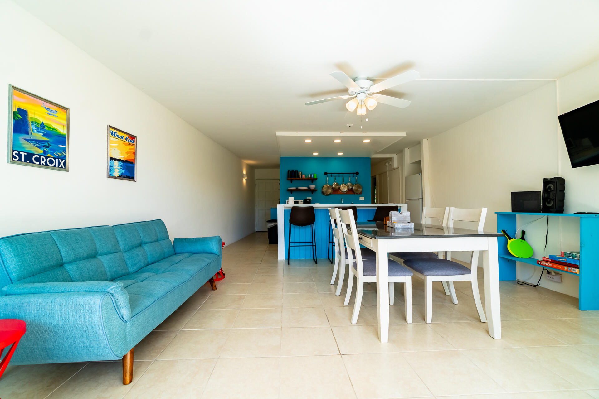 Open-plan living and dining room with a turquoise sofa, white dining set, and bright blue kitchen island.